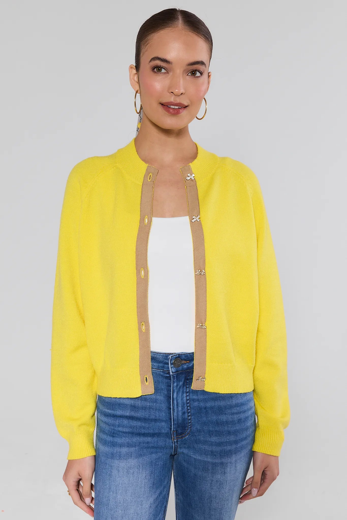 Woman wearing a yellow cardigan over a white top and blue jeans on a gray background