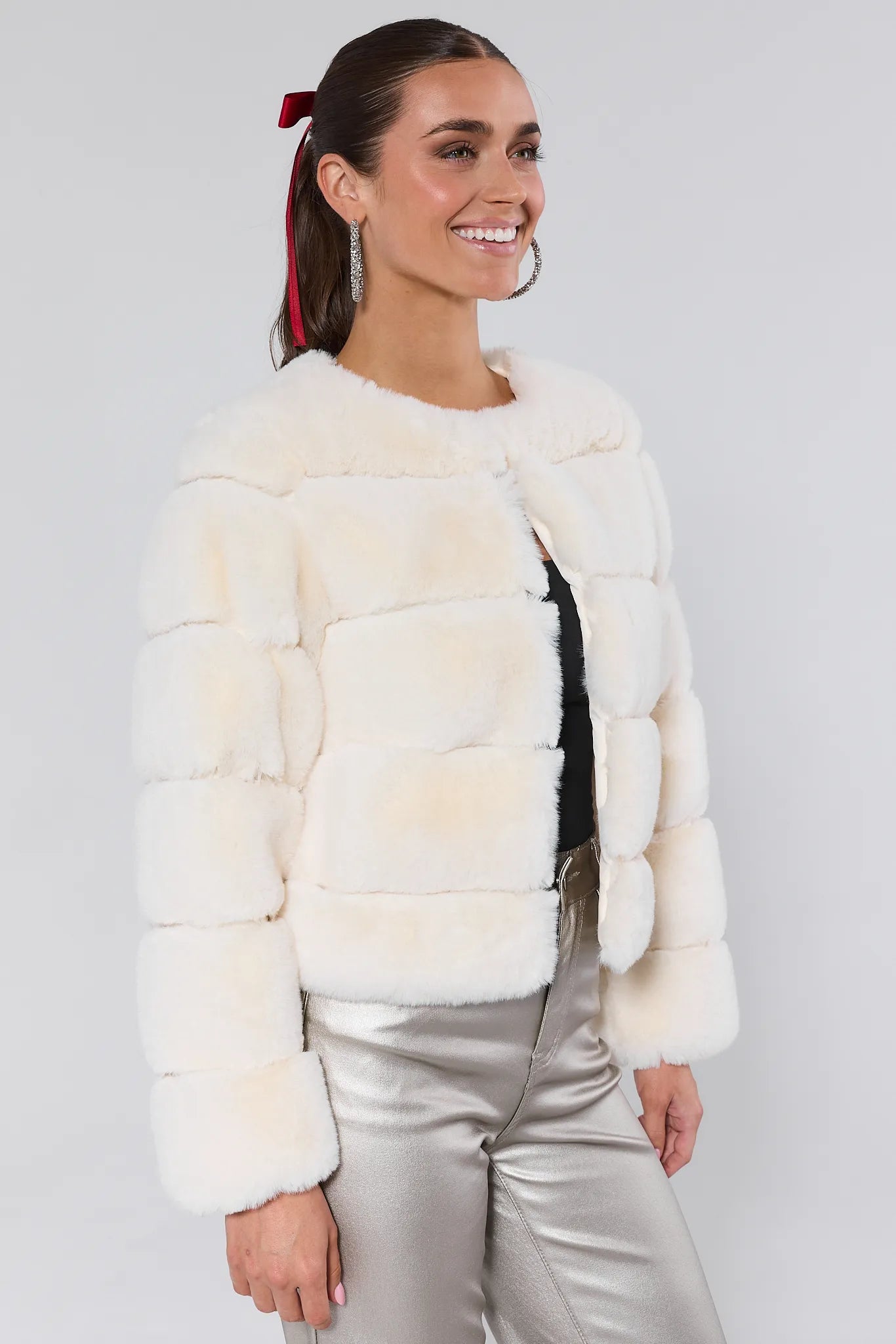 Woman wearing a white fur jacket and silver pants on a plain background