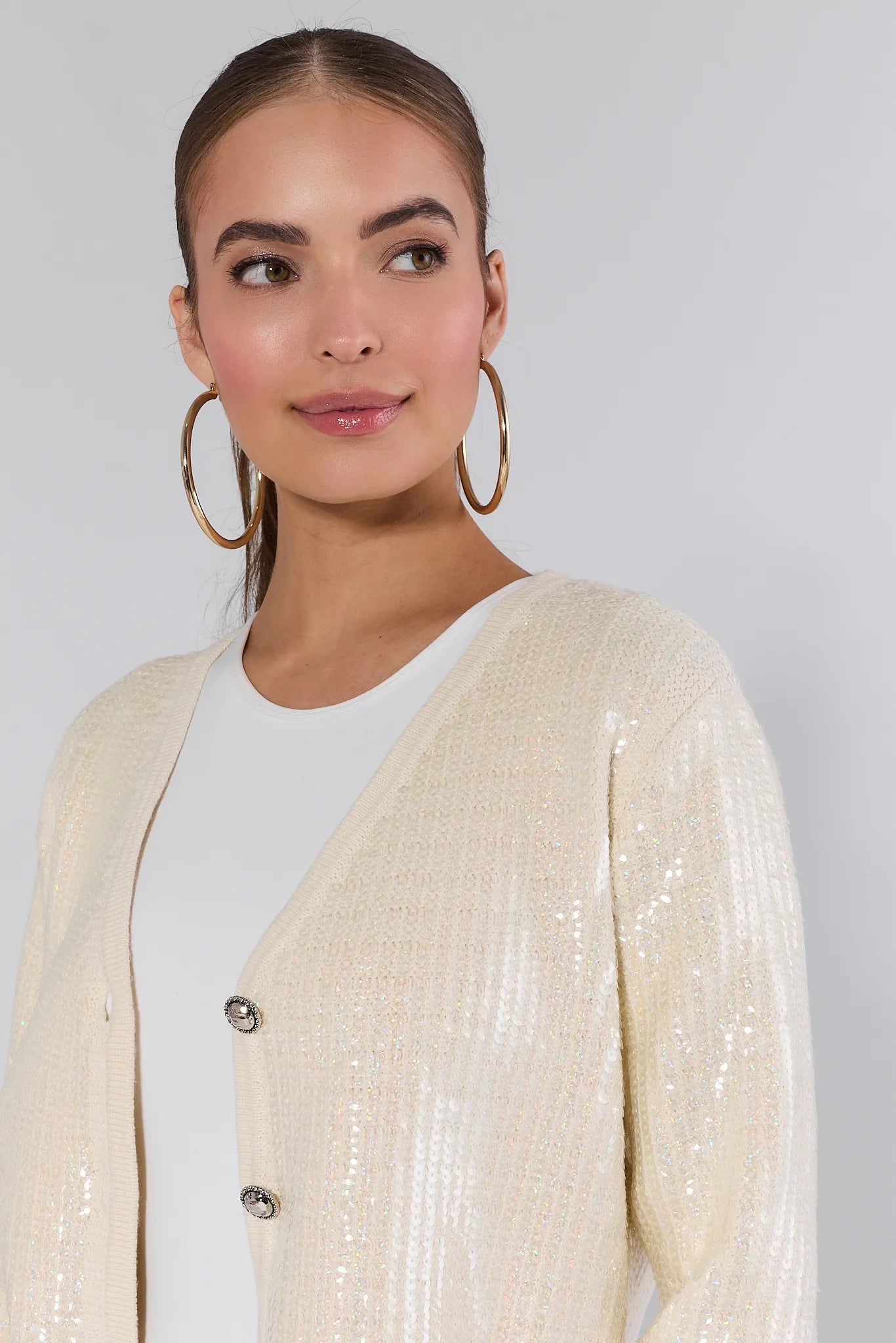 Woman wearing a cream libby cardigan over a white shirt and blue jeans on a plain background