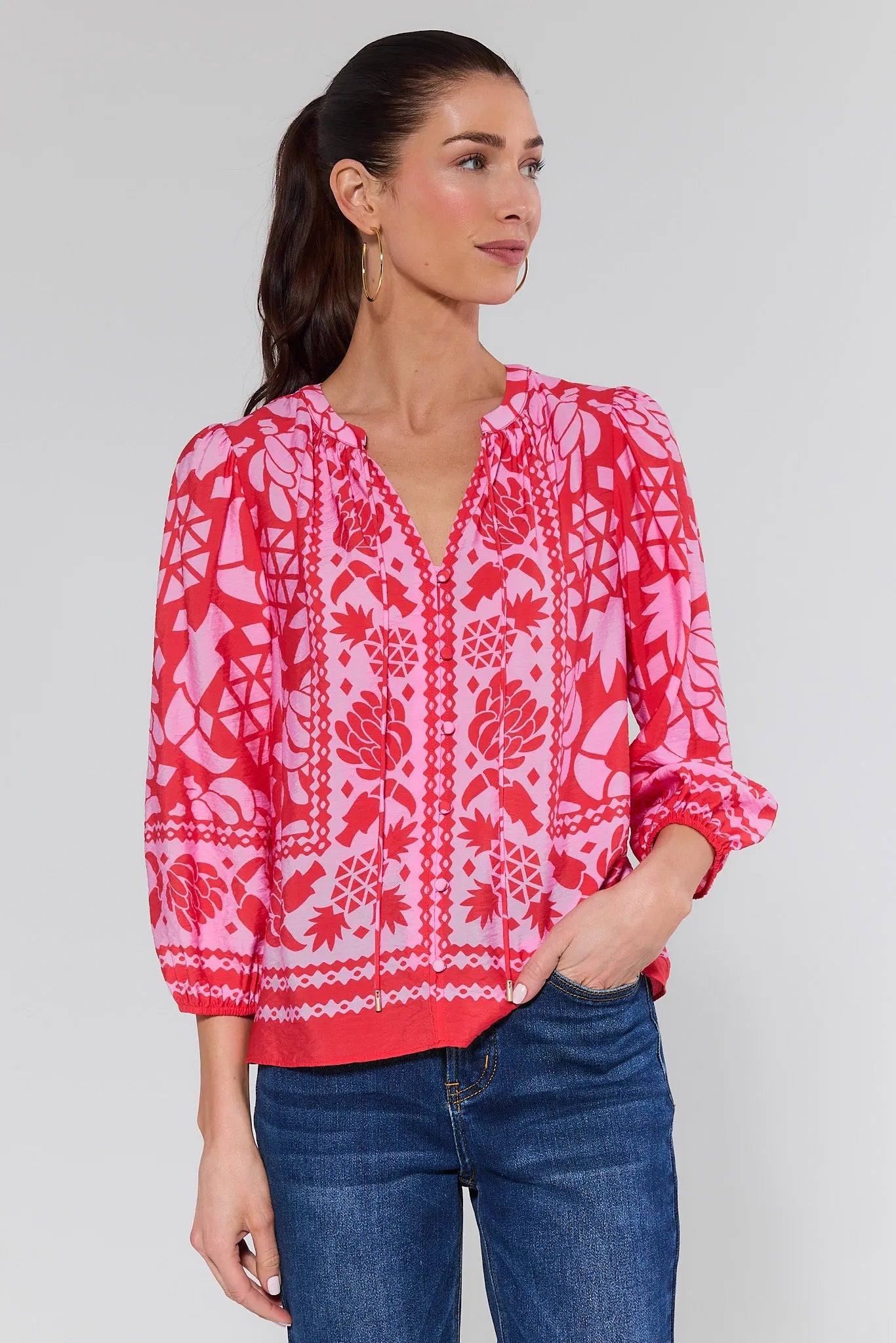 Woman wearing a pink and red patterned blouse with jeans on white background