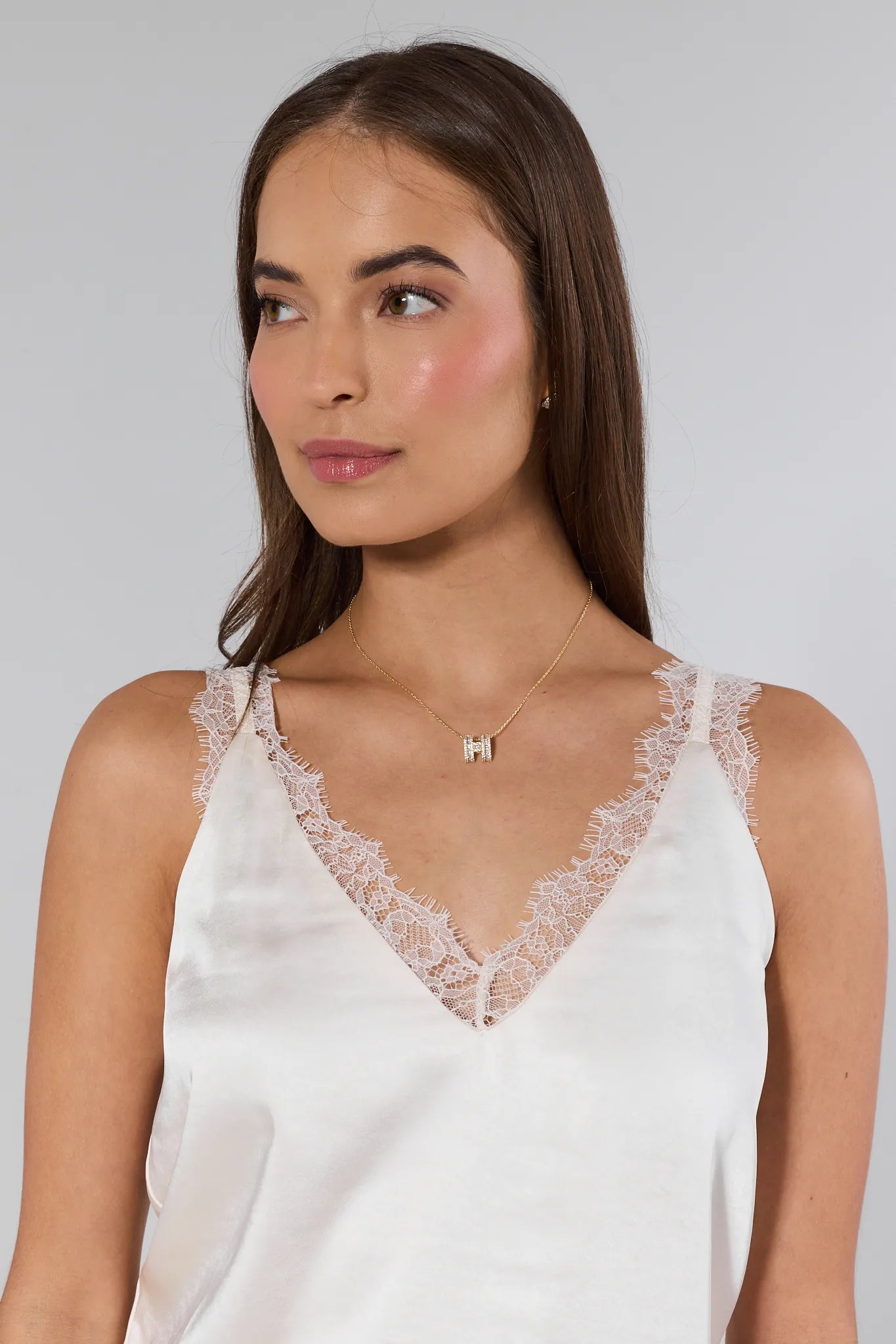 Woman wearing a white lace-trimmed top against a plain background