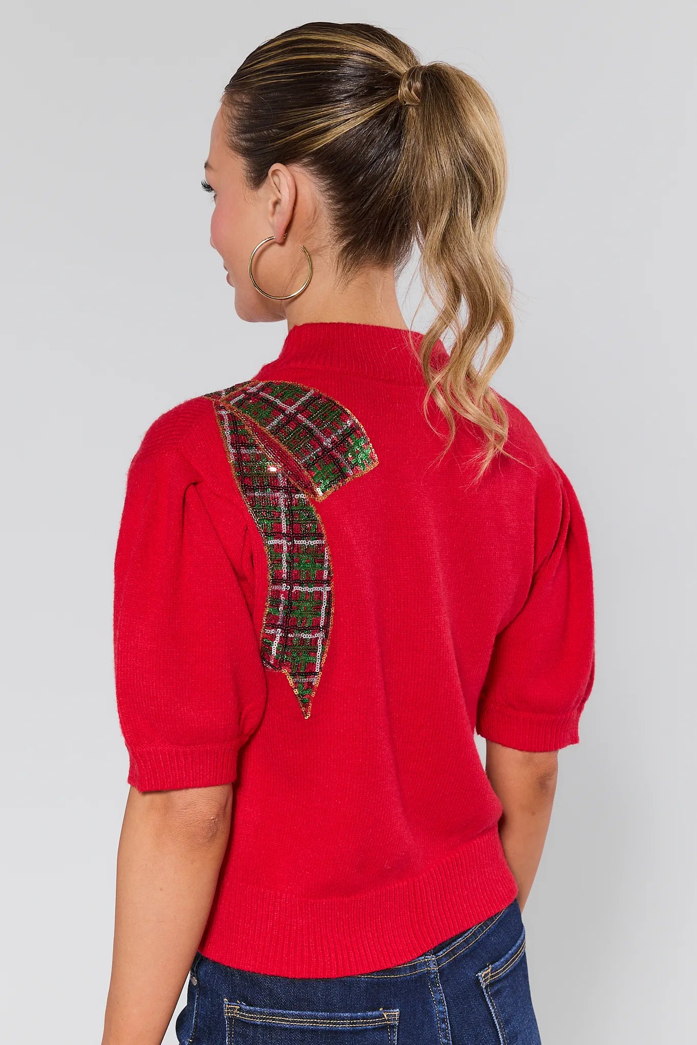 Woman wearing a Eve Red Sequin Bow Sweater on a plain background