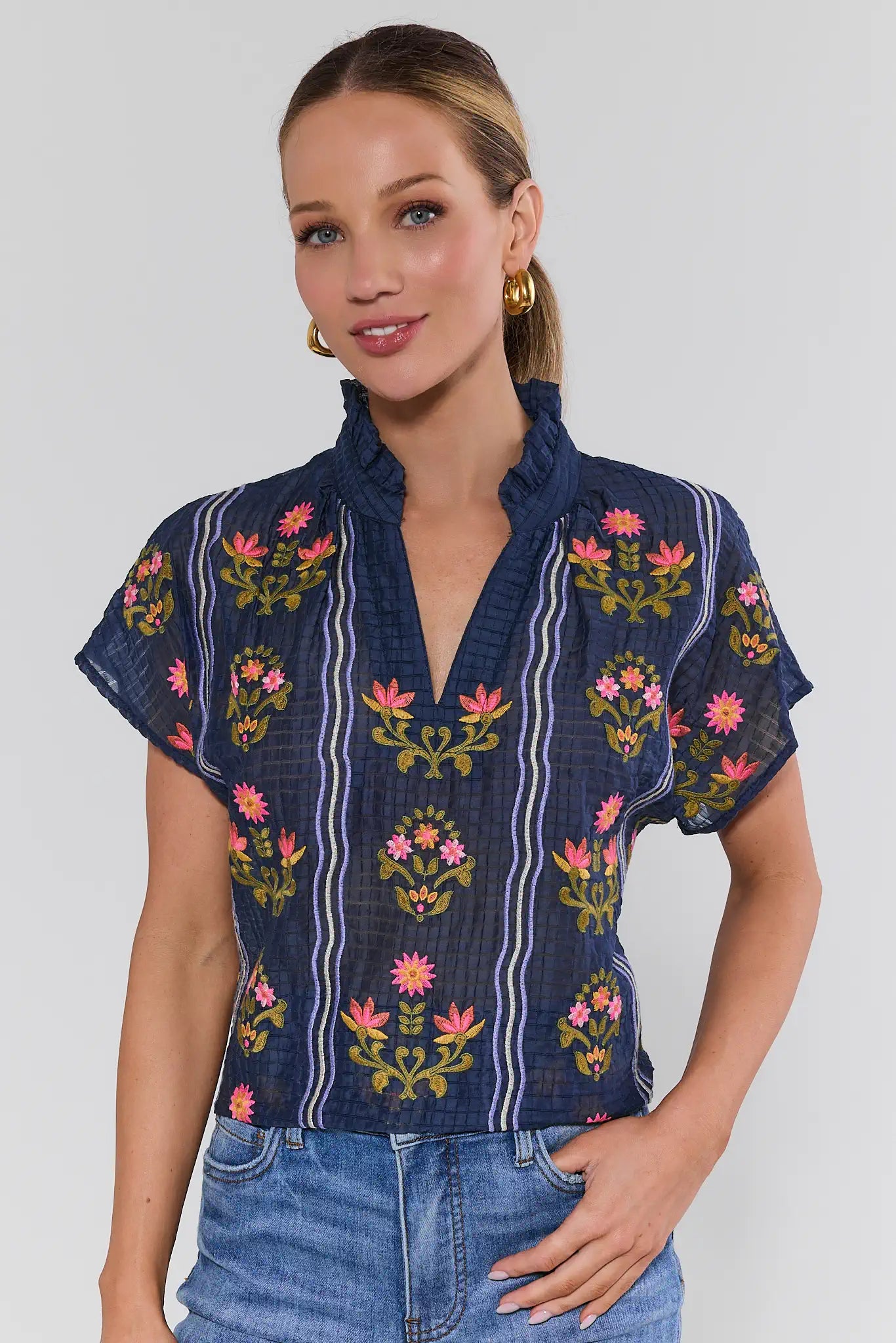 Woman wearing a navy embroidered blouse with floral patterns on a background