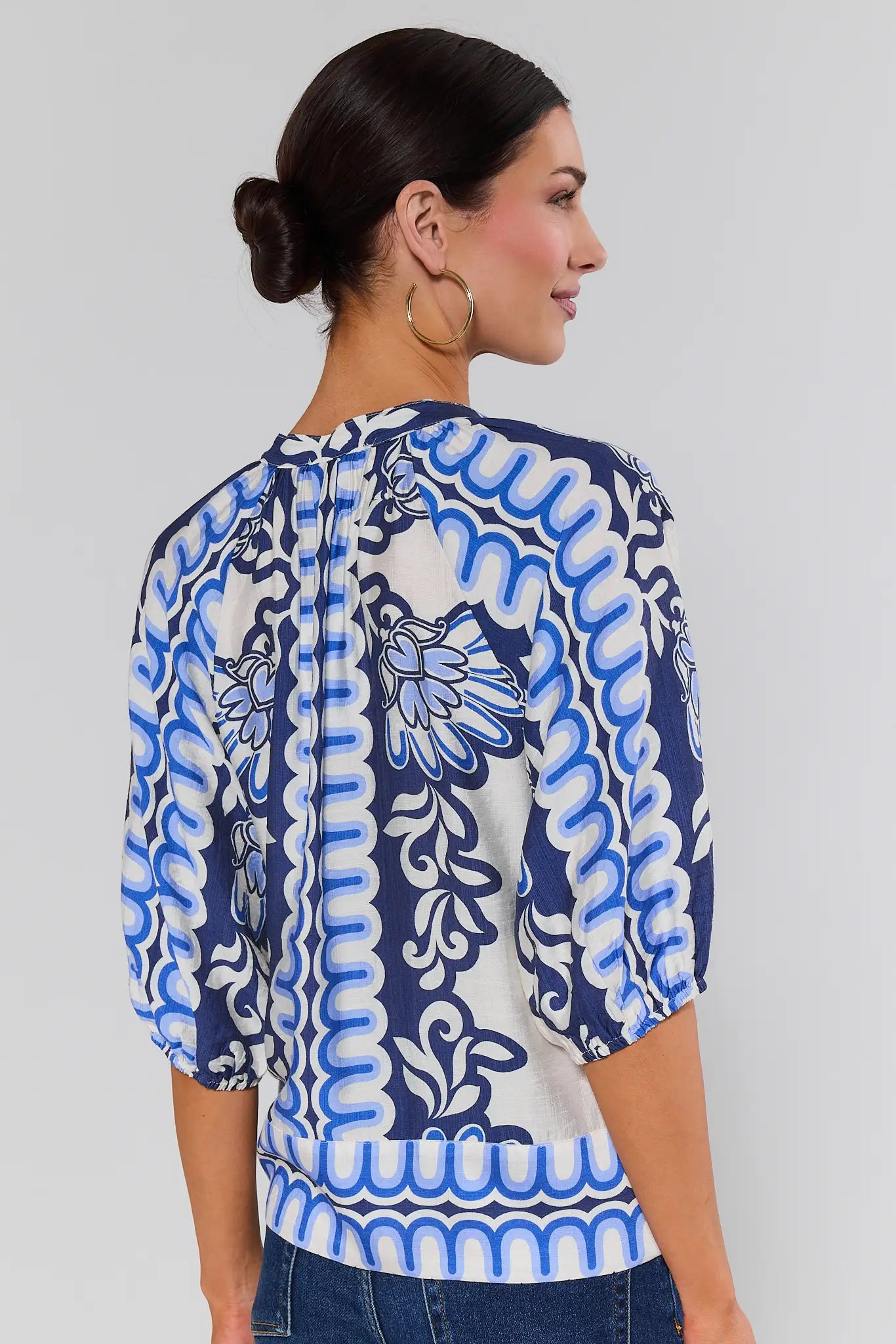 Woman standing wearing a blue and white patterned blouse against a gray background