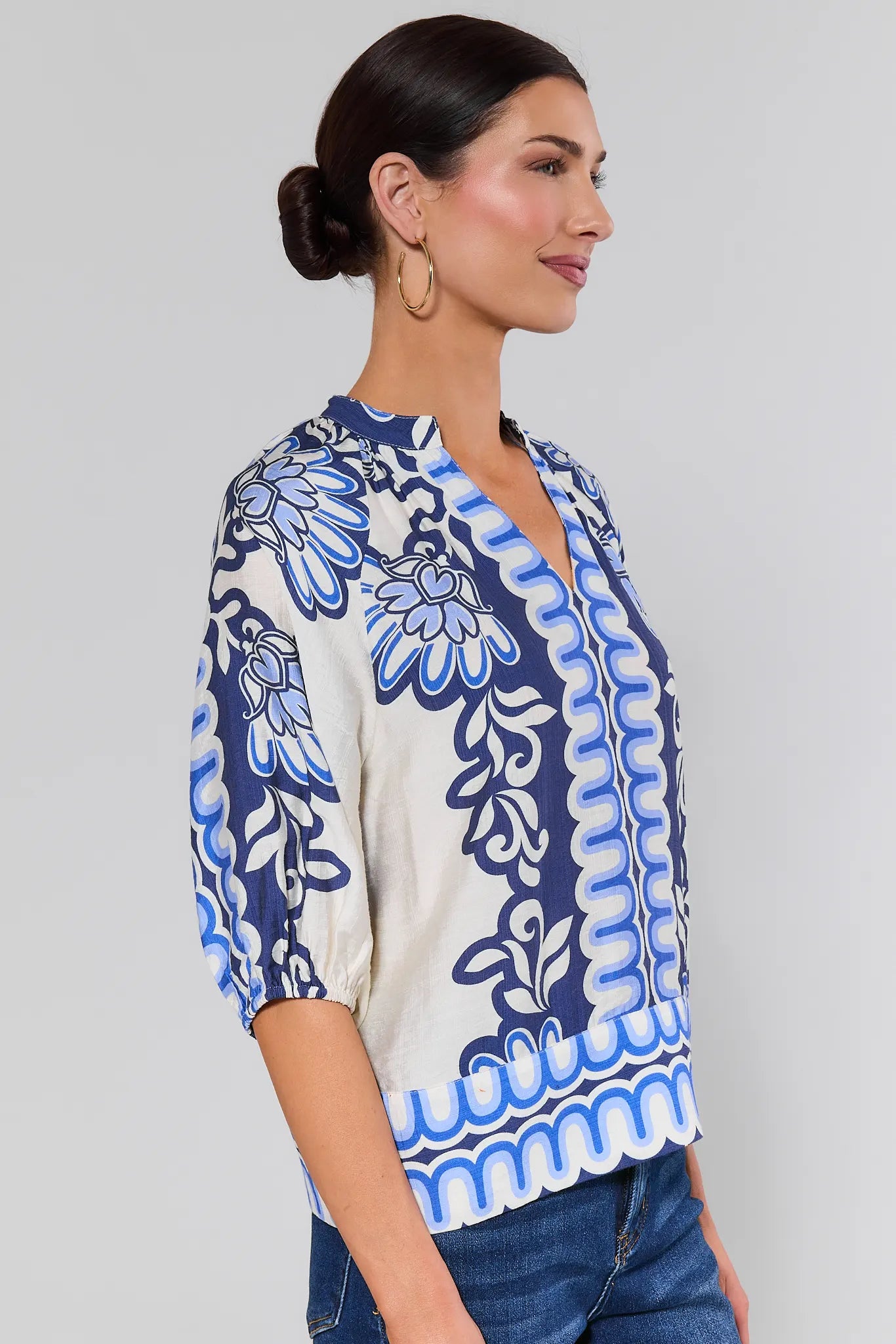 side shot Woman wearing a blue and white patterned blouse against a plain background