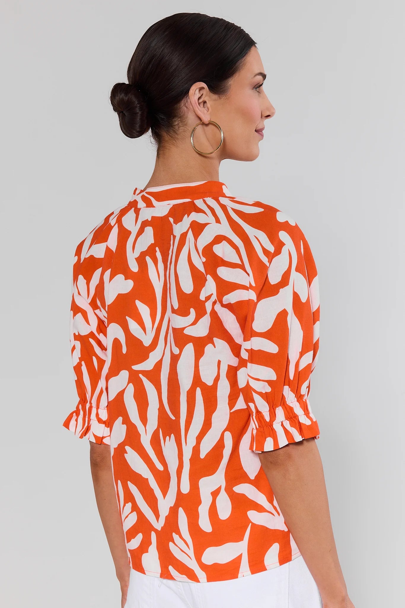Woman standing wearing an orange and white patterned blouse against a plain background