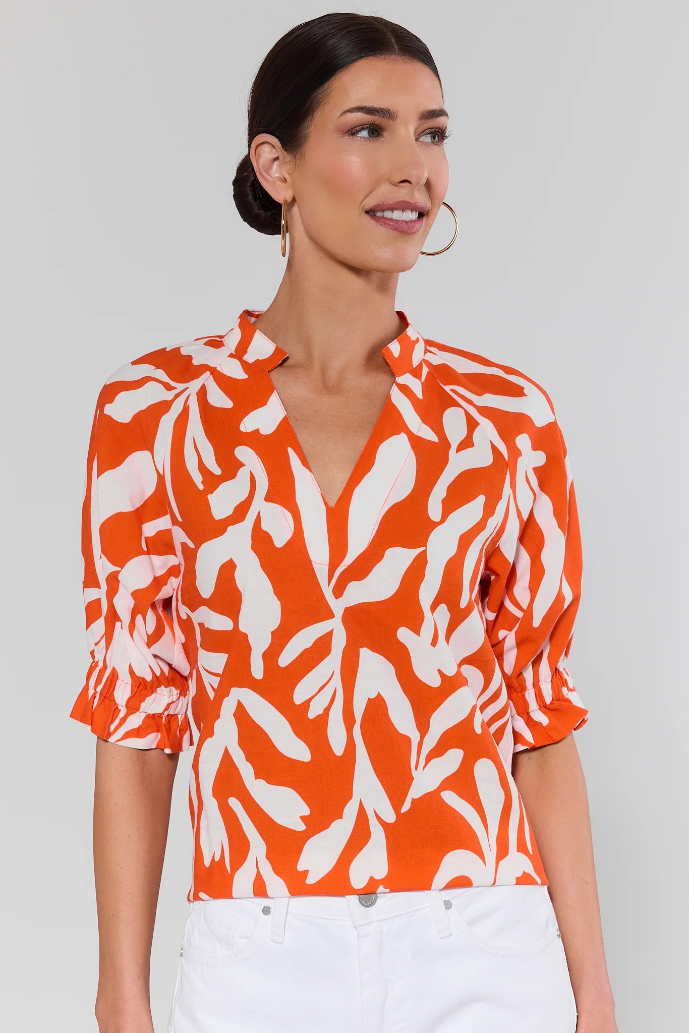 Woman wearing an trish orange and white patterned blouse against a background