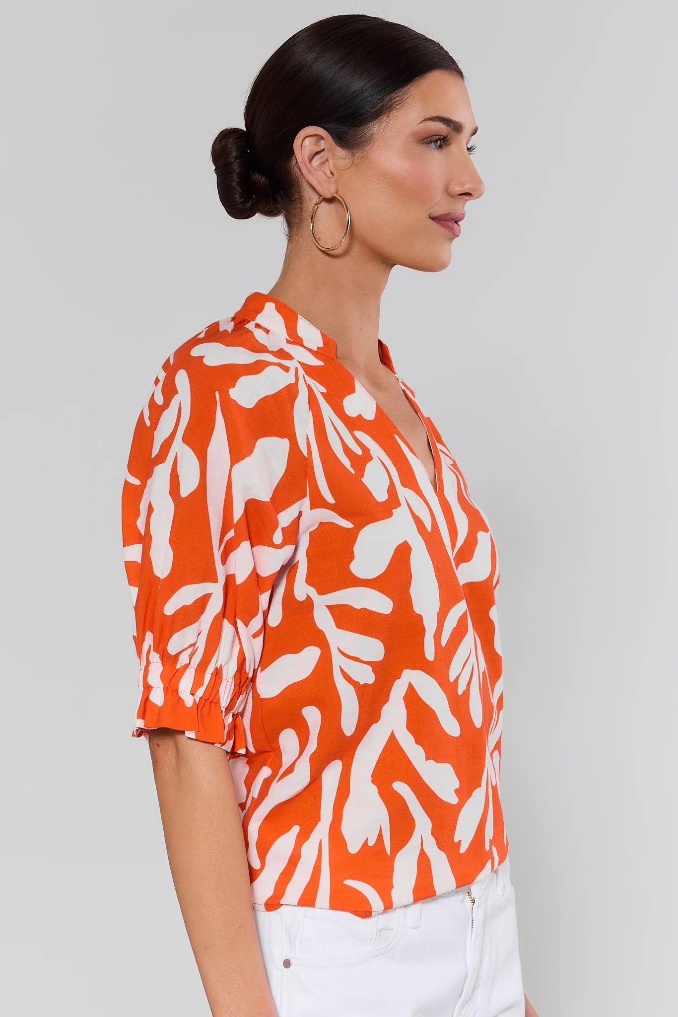 side shot Woman wearing an orange and white patterned blouse against a plain background