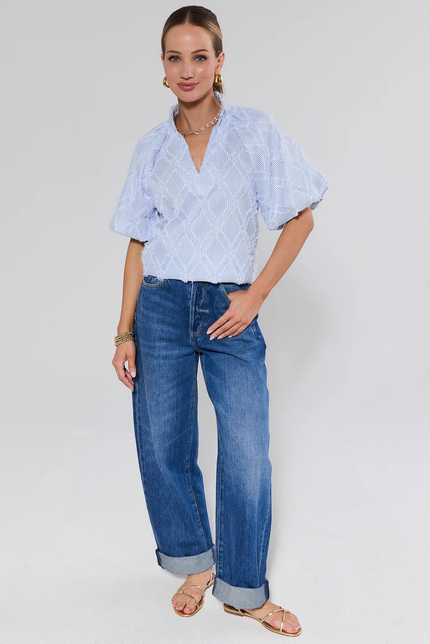 Woman wearing a light patterned shirt and blue jeans on a background