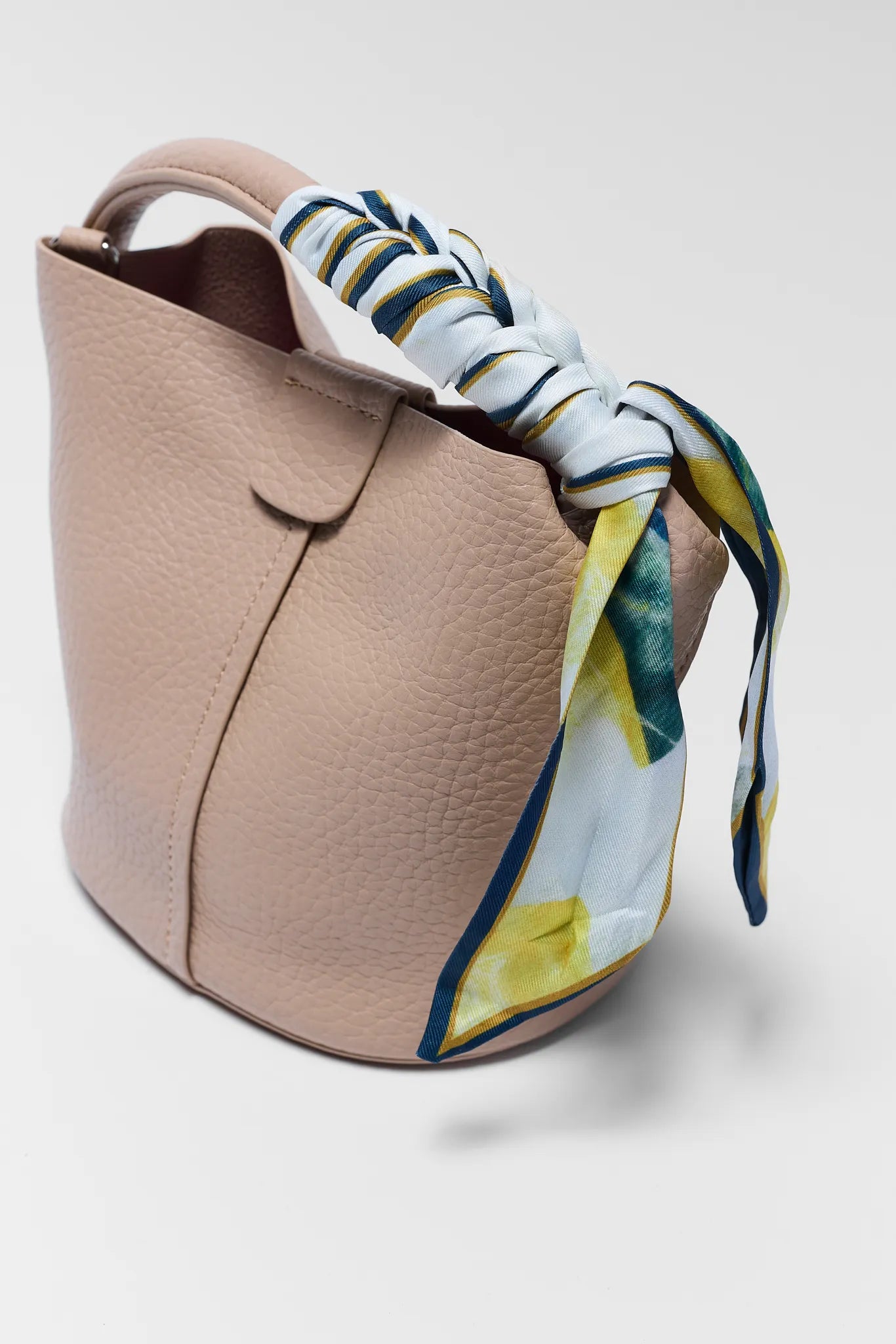 Beige handbag with a floral scarf tied around it on a light gray background