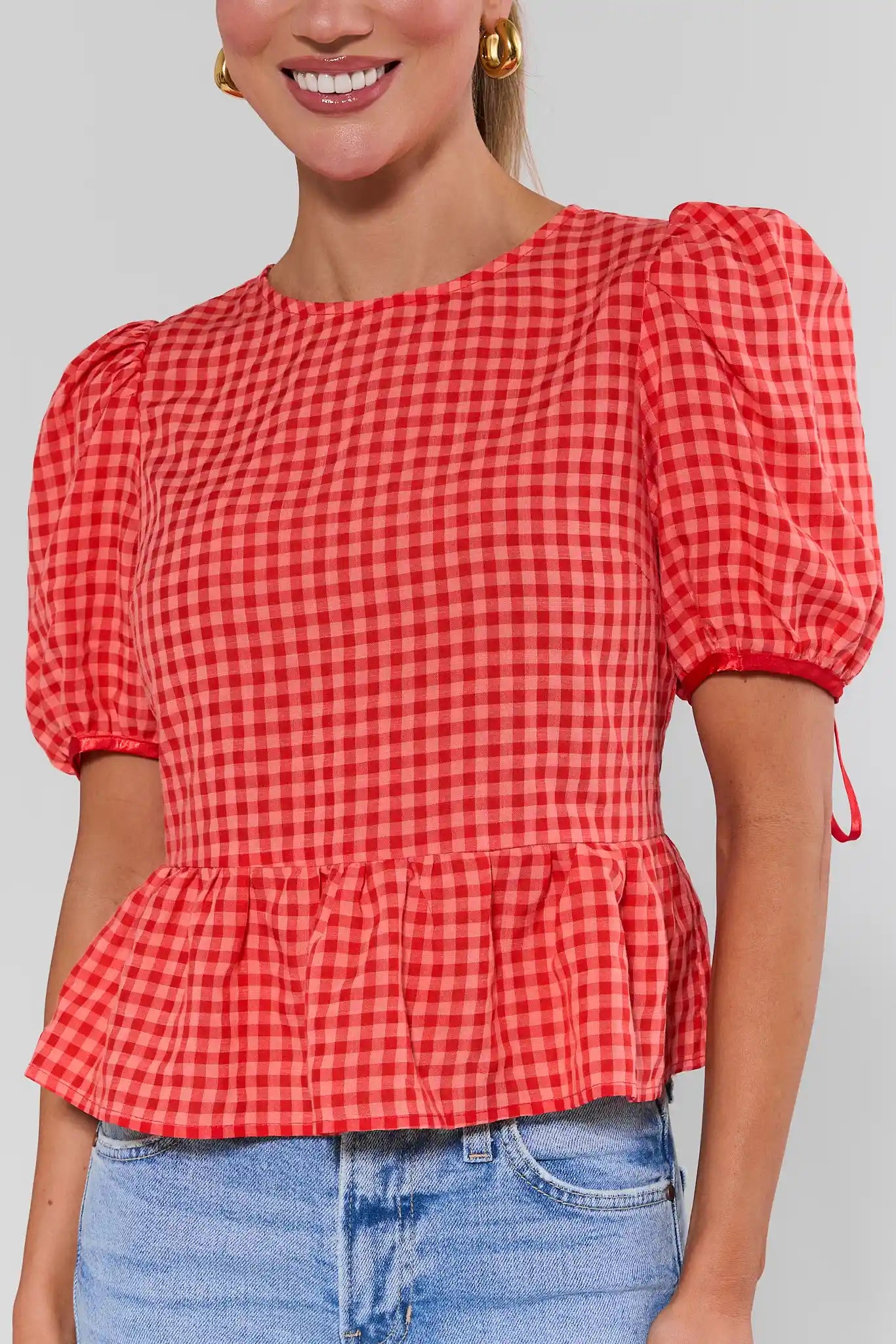close up Woman wearing a red checkered blouse with puff sleeves against a gray background