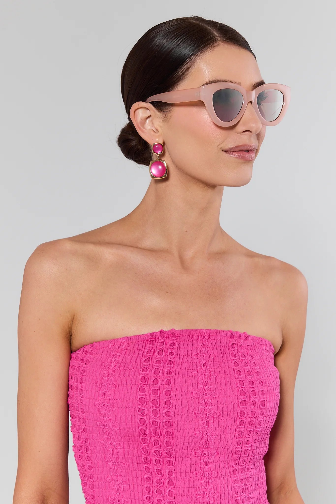 Woman wearing a pink strapless dress and sunglasses with a gray background