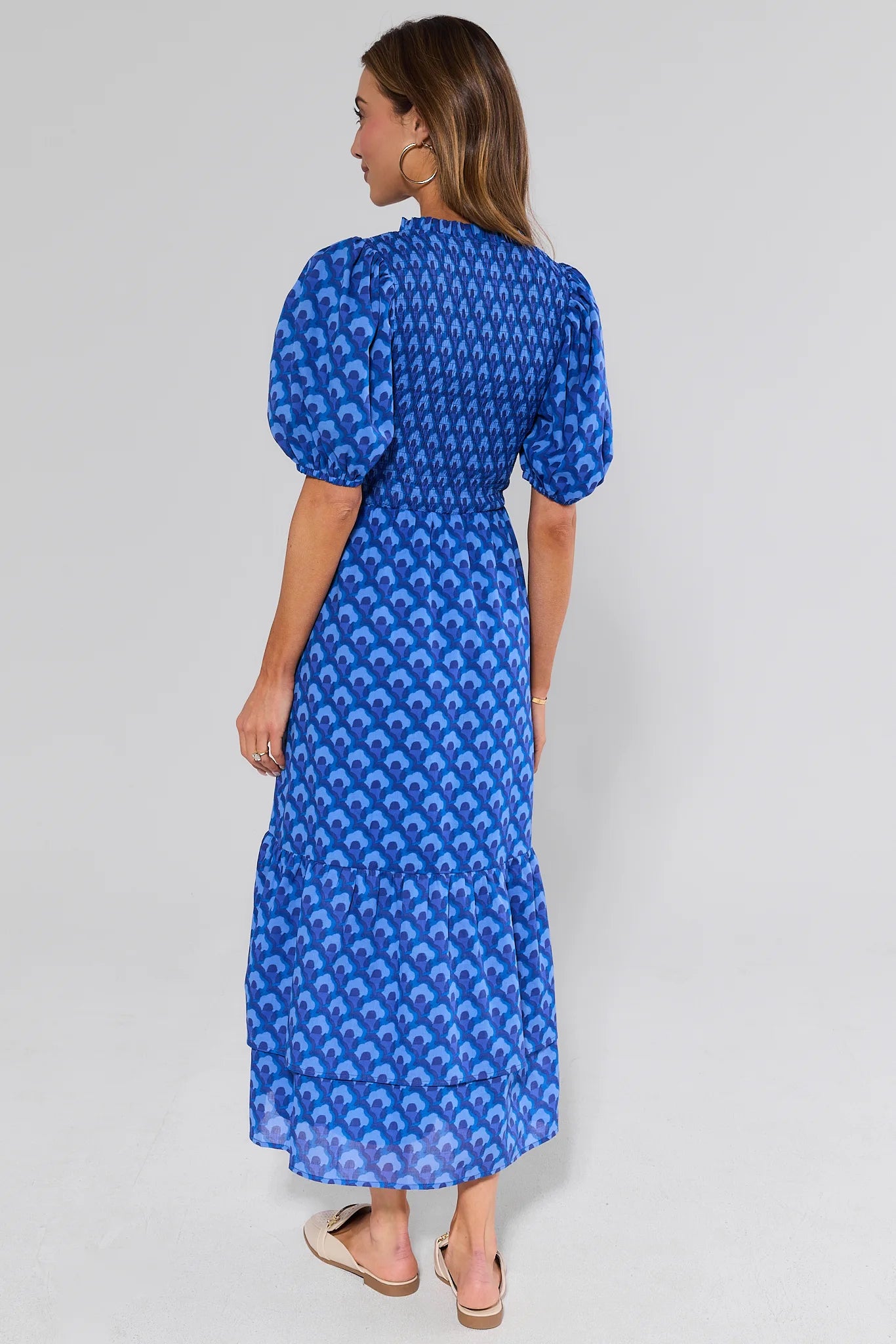 Woman standing wearing a blue patterned dress on a gray background