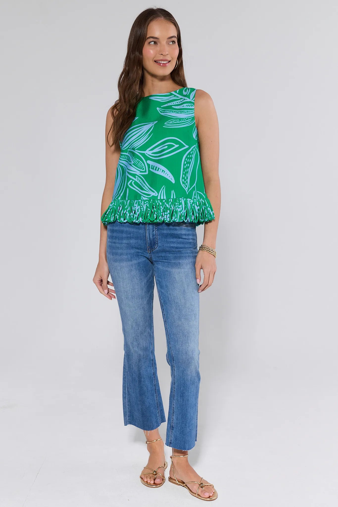 Woman wearing a green leaf-patterned top and blue jeans on a white grey background