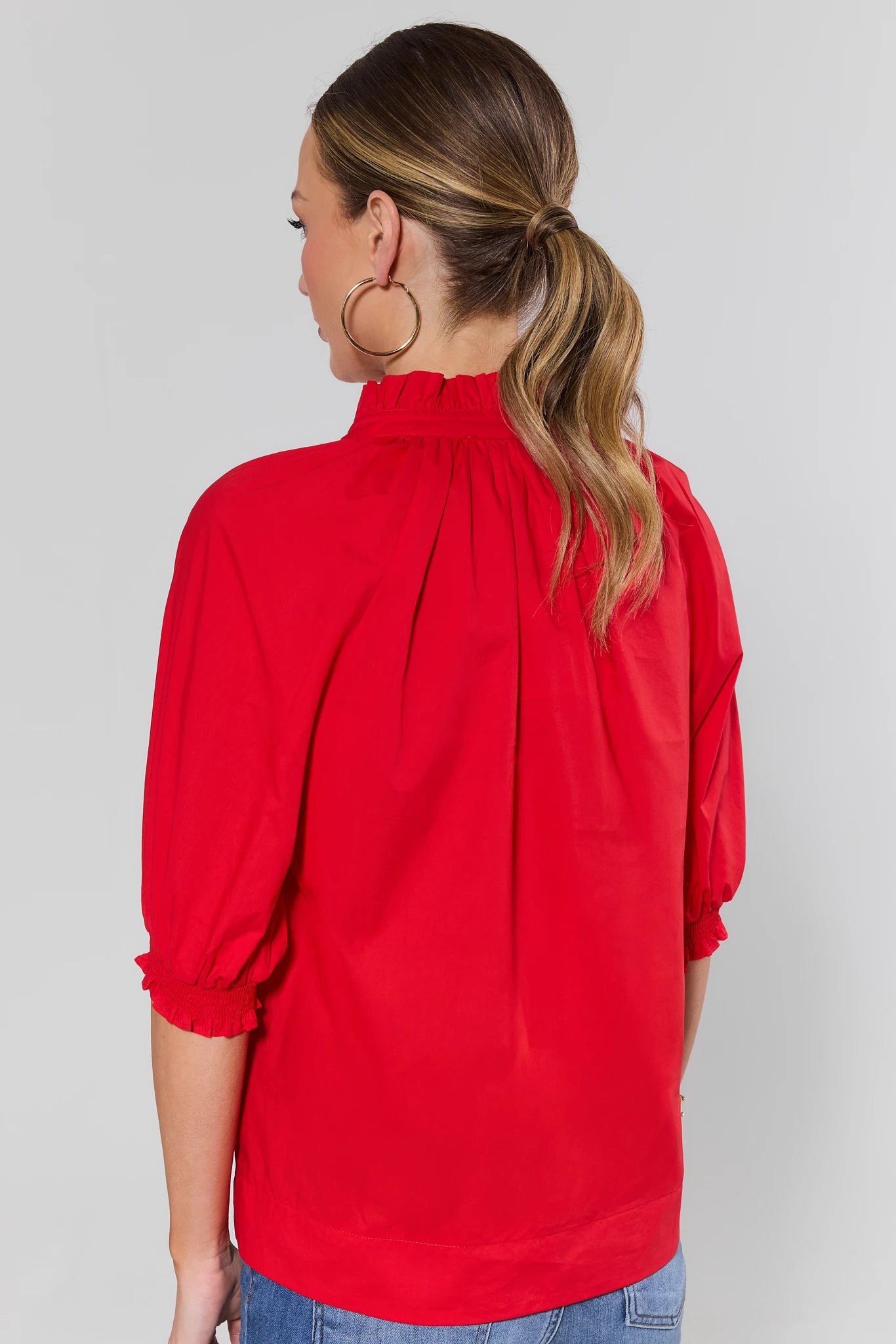 Woman standing wearing a red blouse with a plain background