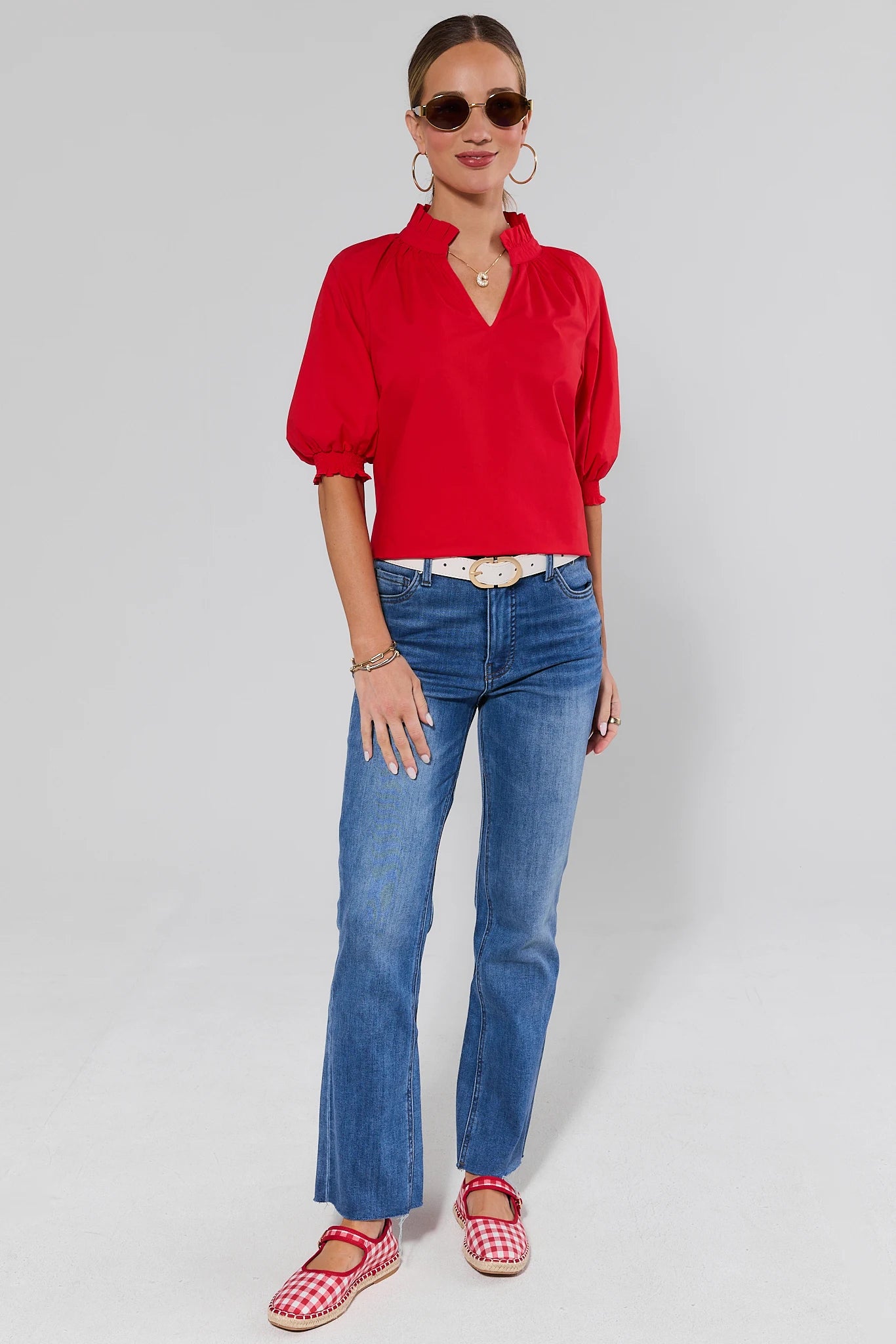 Woman wearing a red blouse, blue jeans, and red checkered shoes on a white background
