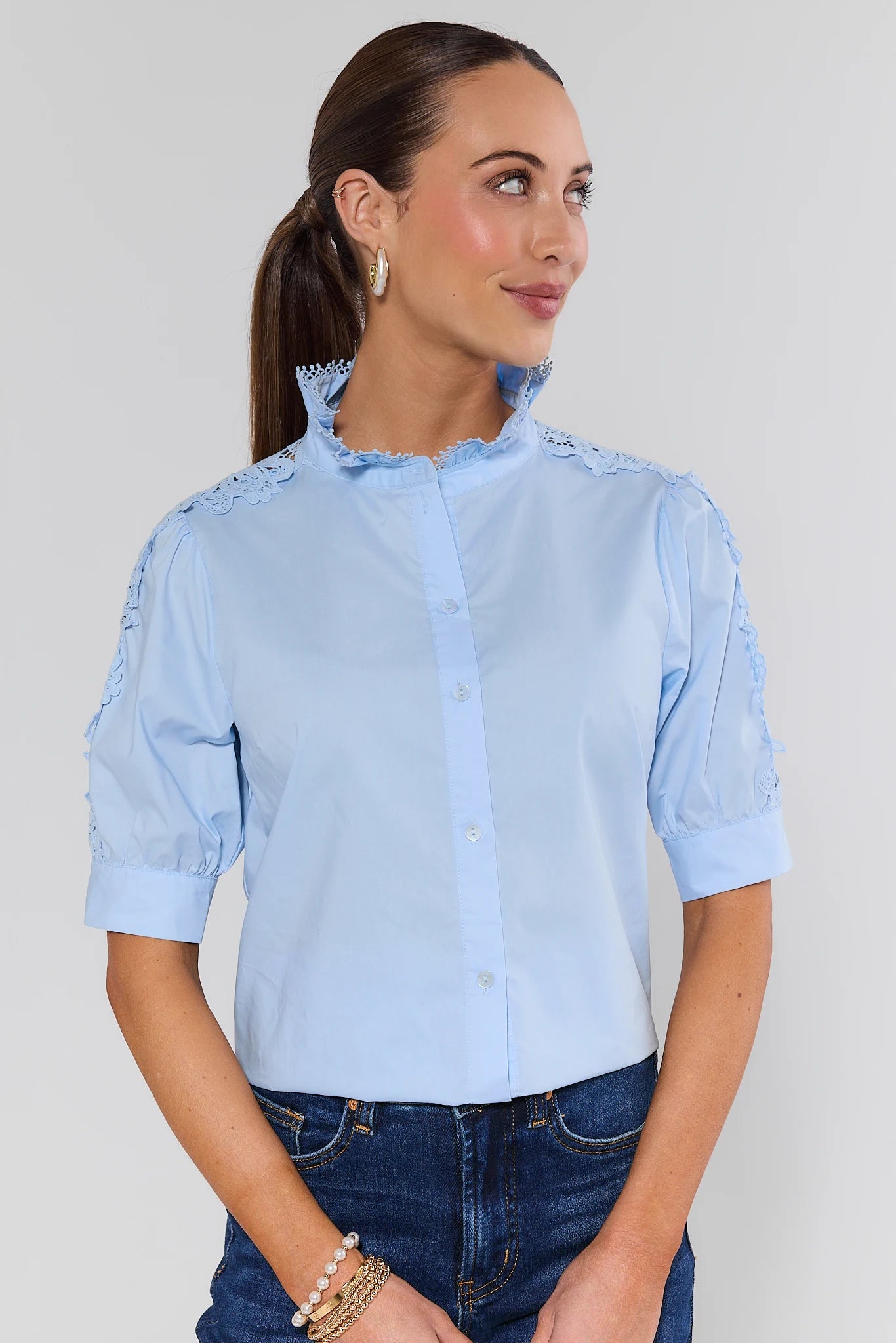 Woman wearing a light blue shirt with ruffled details on a plain background