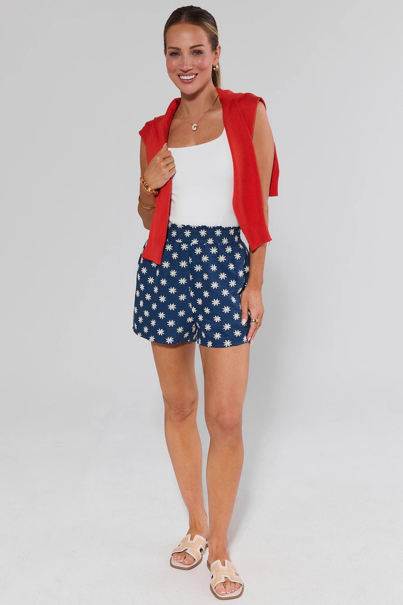 Woman wearing a red cardigan, white top, and blue shorts with white stars on a light gray background