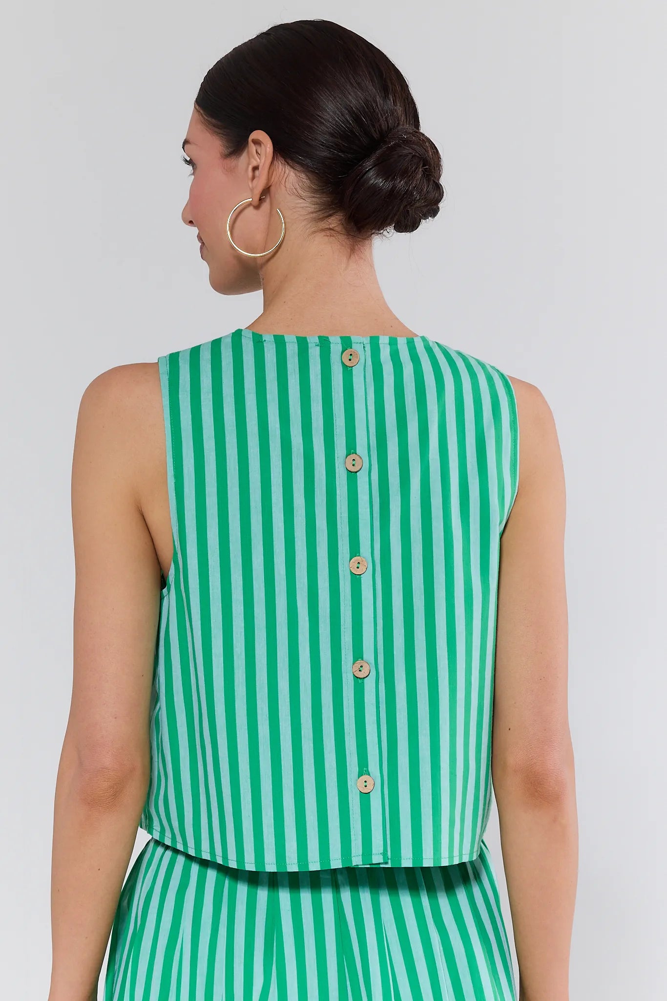 Woman wearing a green and white striped sleeveless top with buttons on a plain background
