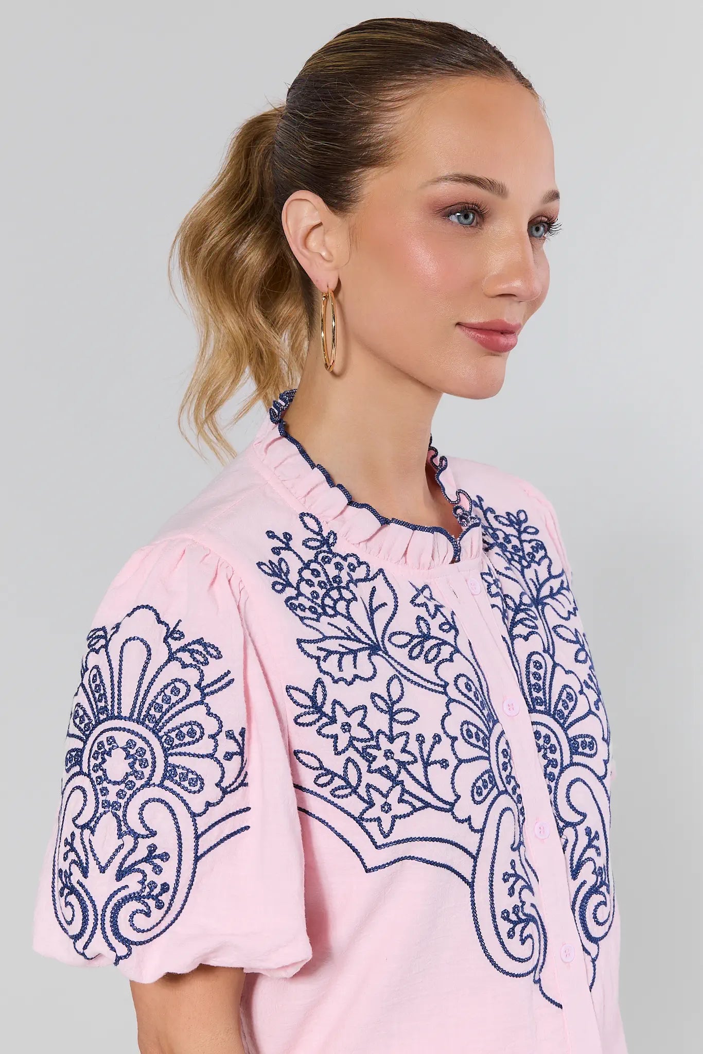 close up of Woman wearing a pink blouse with blue embroidery on a plain background