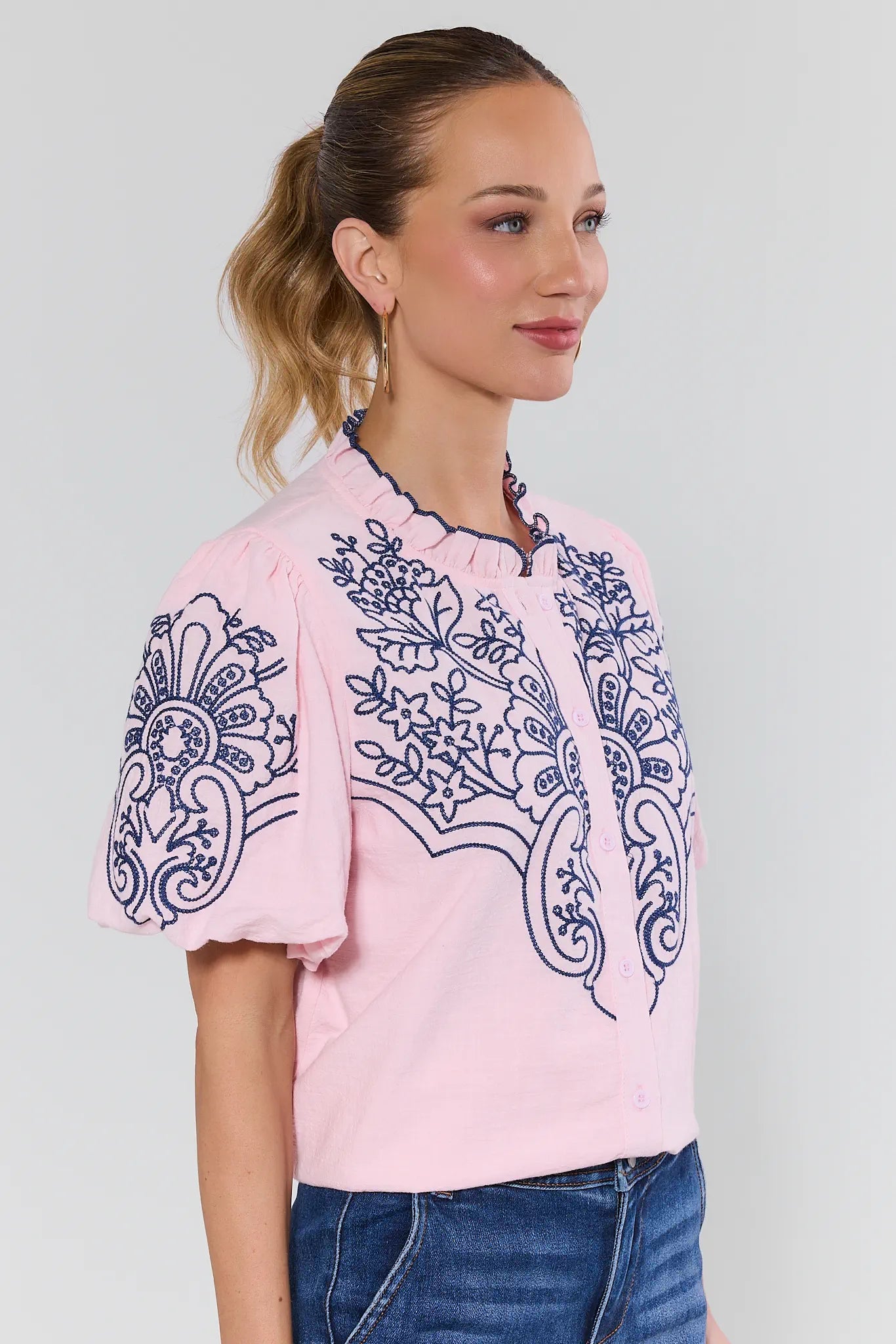 Woman wearing a pink blouse with blue embroidery on background