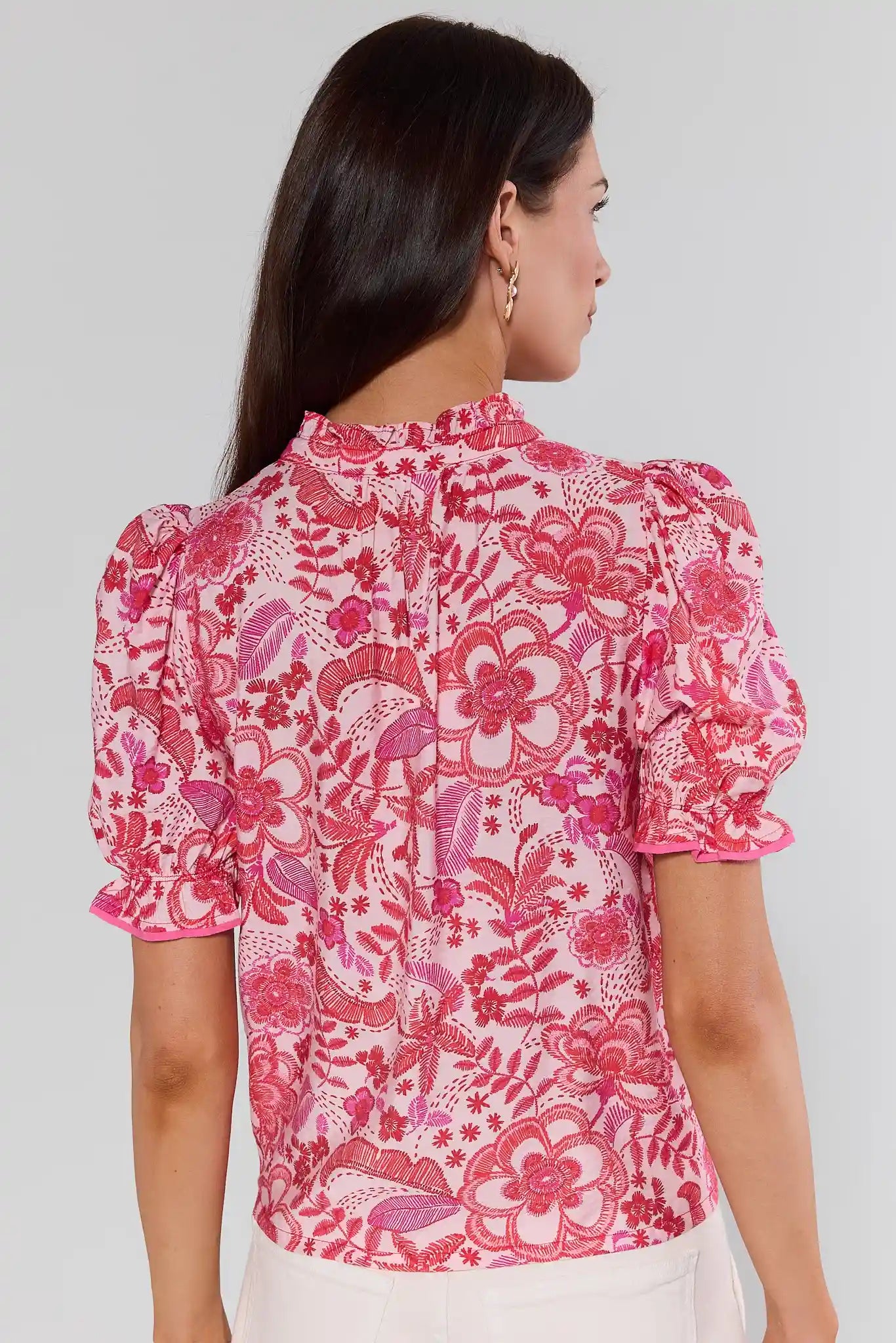 Woman standing wearing a pink floral blouse against a gray background