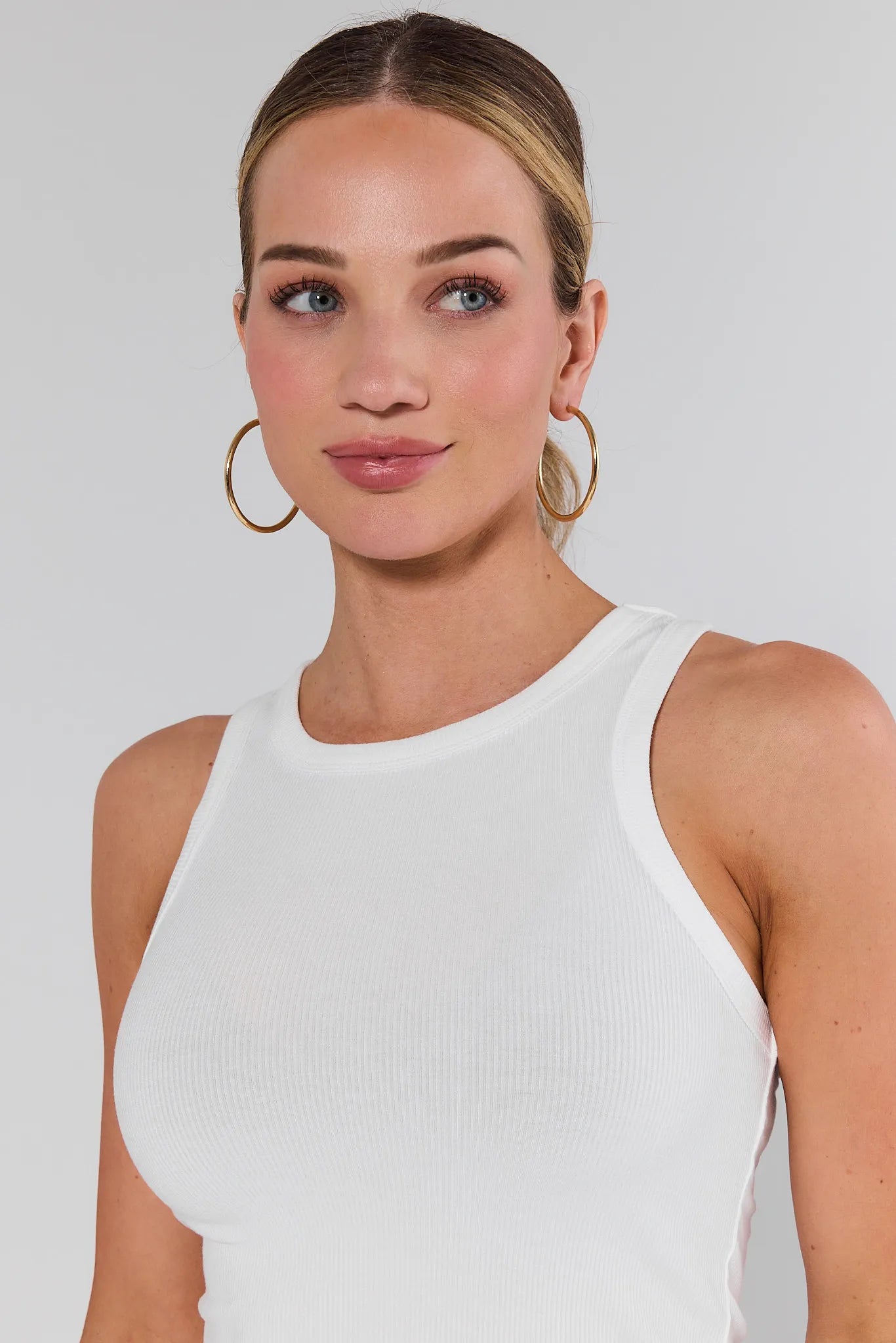 Woman wearing a white sleeveless top against a plain background