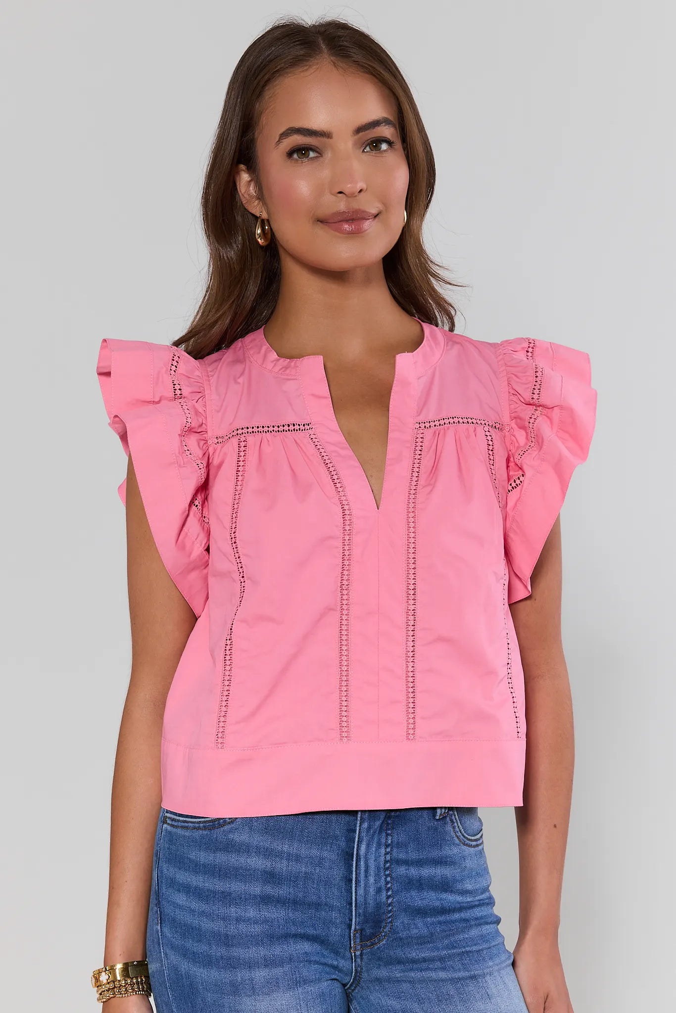 Woman wearing a pink blouse with ruffled sleeves on a gray background