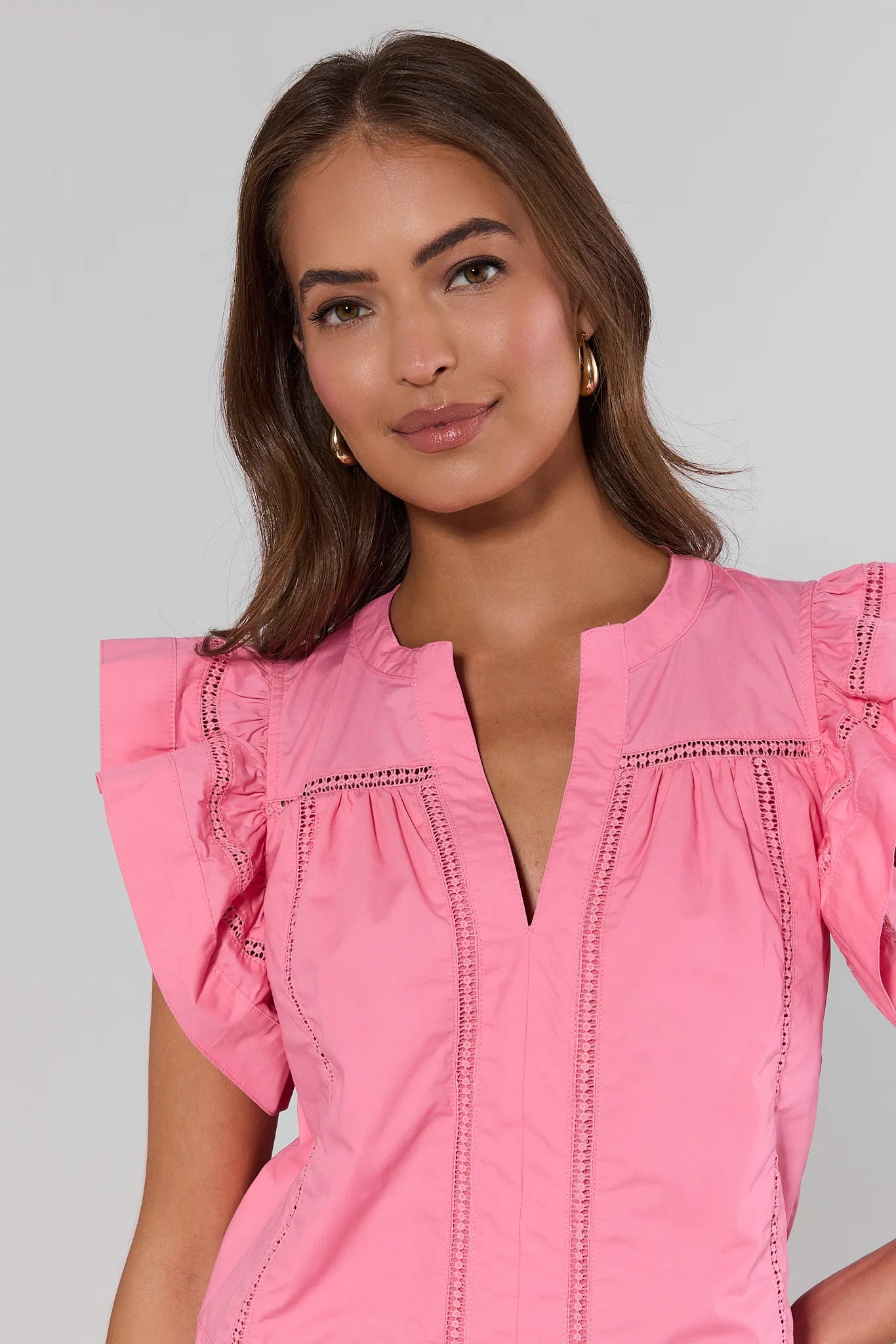 close up Woman wearing a pink blouse with ruffled sleeves against a plain background