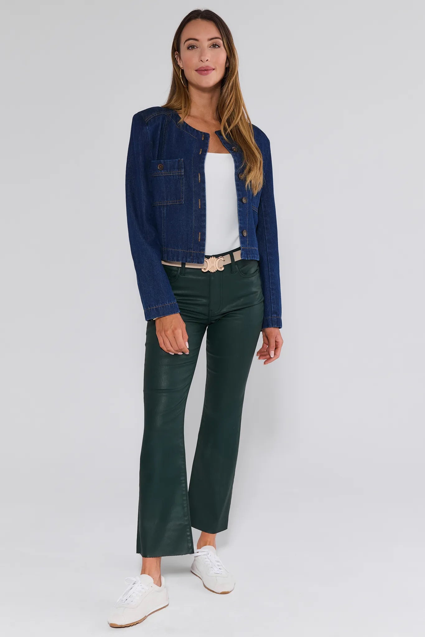 Woman wearing a blue denim jacket, white top, green Kelsey Jeans Wax Coated, and white shoes on a light gray background