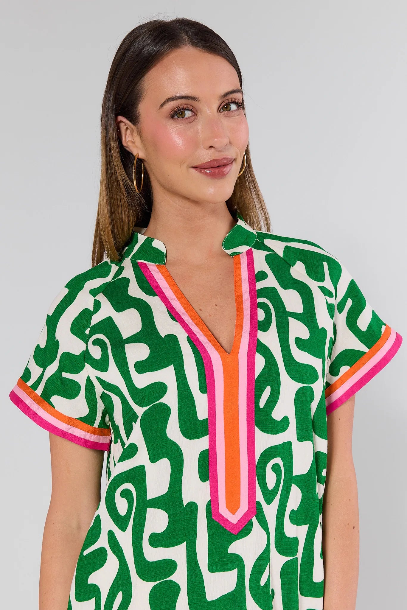 Woman wearing a green patterned top with pink accents on a gray background