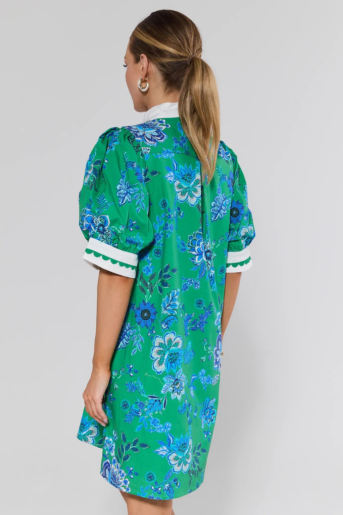 Woman wearing a green floral dress with white trim on a plain background