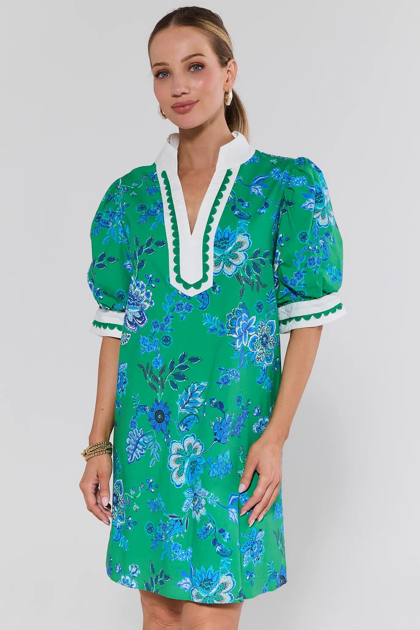 Woman wearing a green floral dress with white trim on a plain background