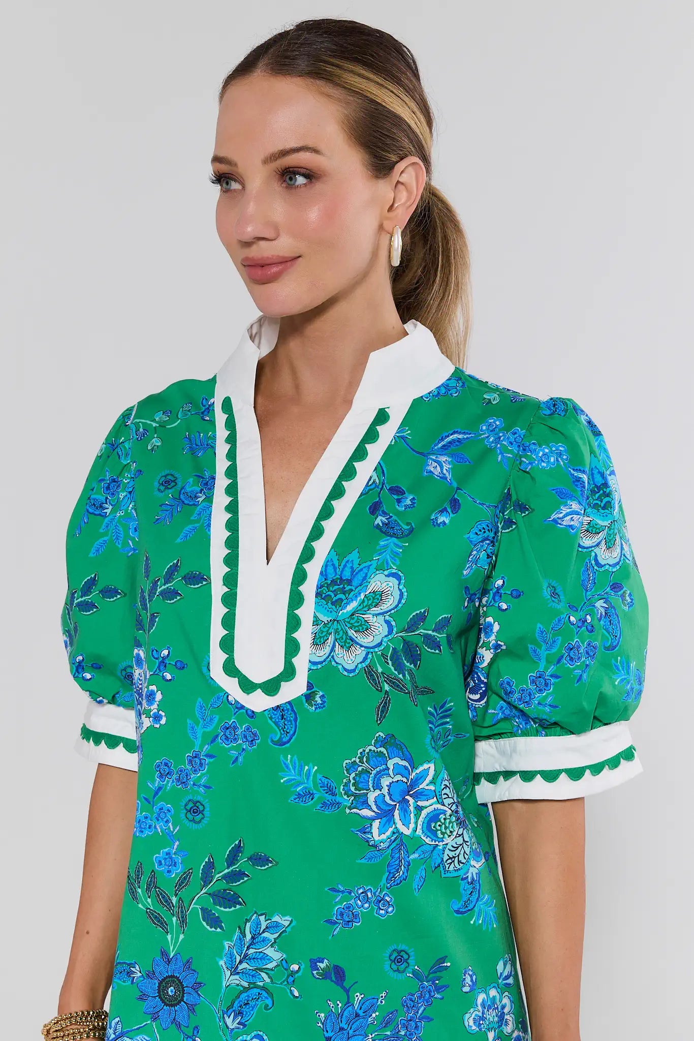 Woman wearing a green floral dress with white trim on a plain background
