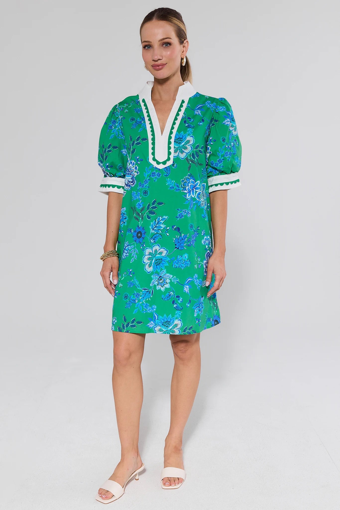 Woman wearing a green floral dress with white trim on a gray background