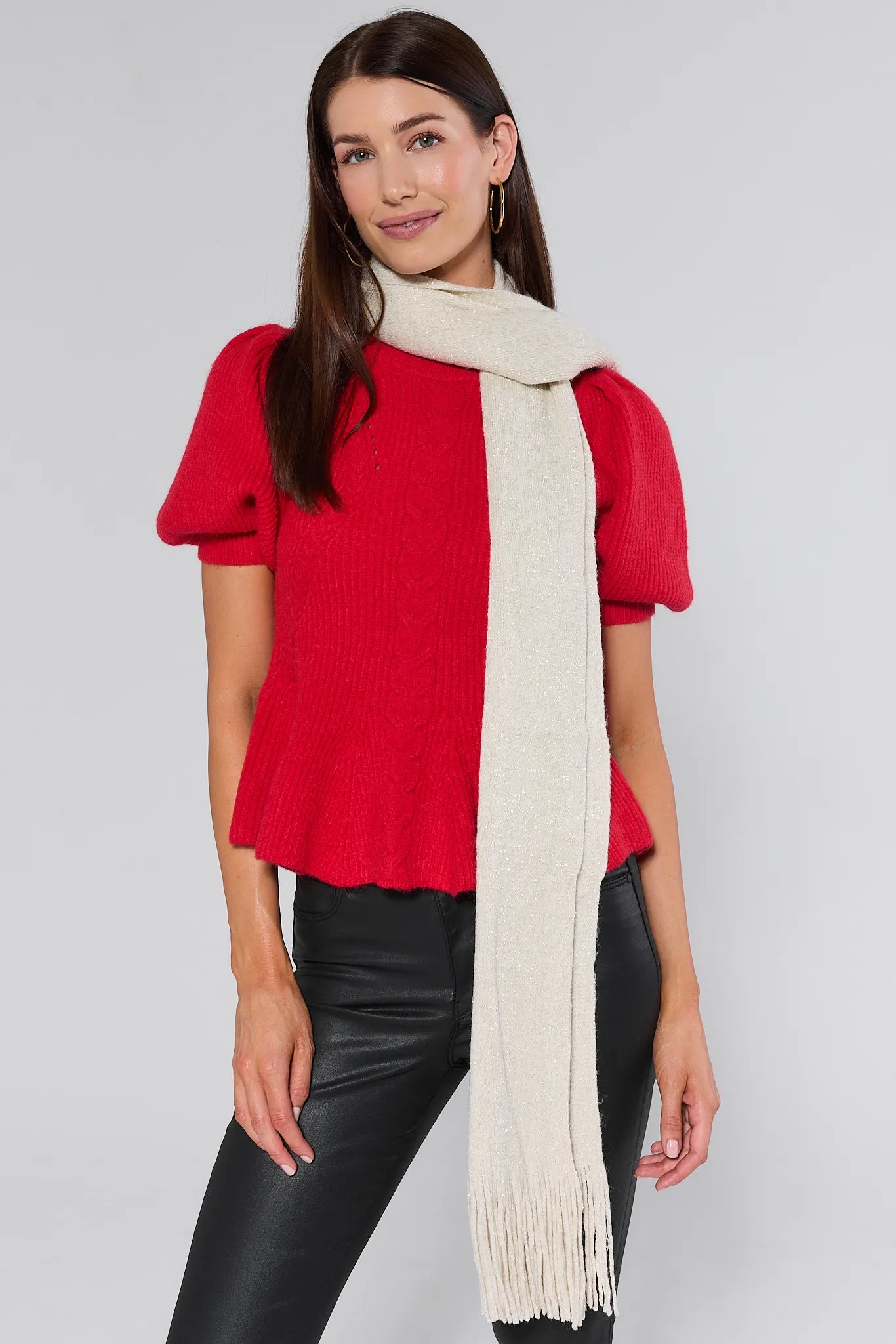 Woman wearing a red sweater and black pants with a Karris Cream Fringe Scarf on a plain background