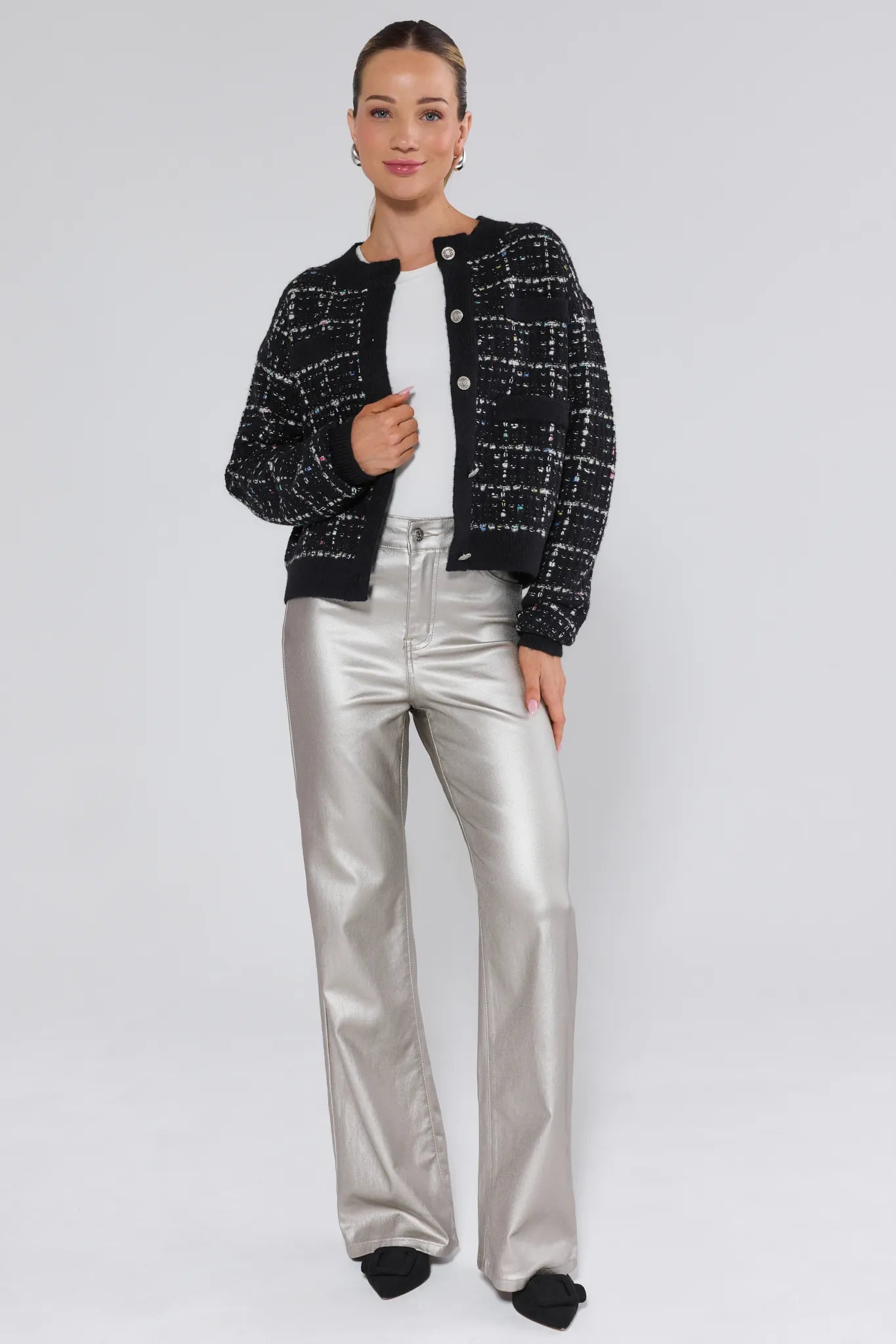 Woman wearing a black tweed jacket and silver pants on a white background