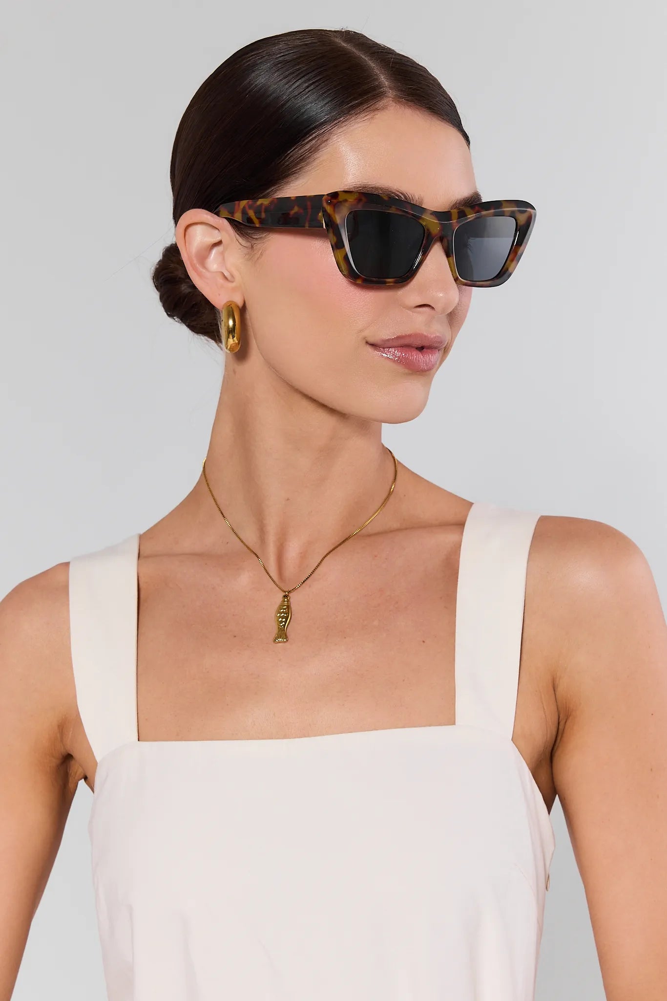 Woman wearing tortoiseshell sunglasses with a plain background