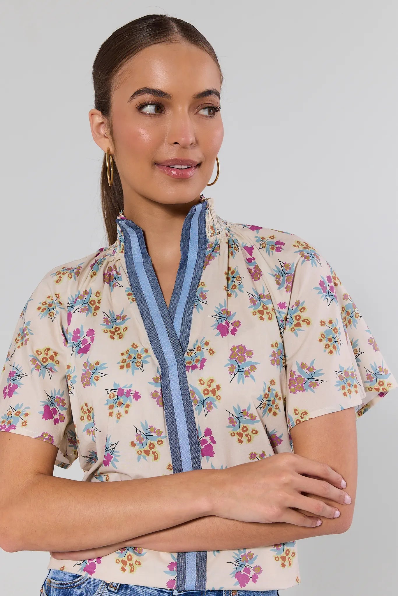 Young woman models the Macey Cream Floral Print Top by THML, featuring a floral pattern, stand-up collar, denim-tone trim, and smocked short sleeves.