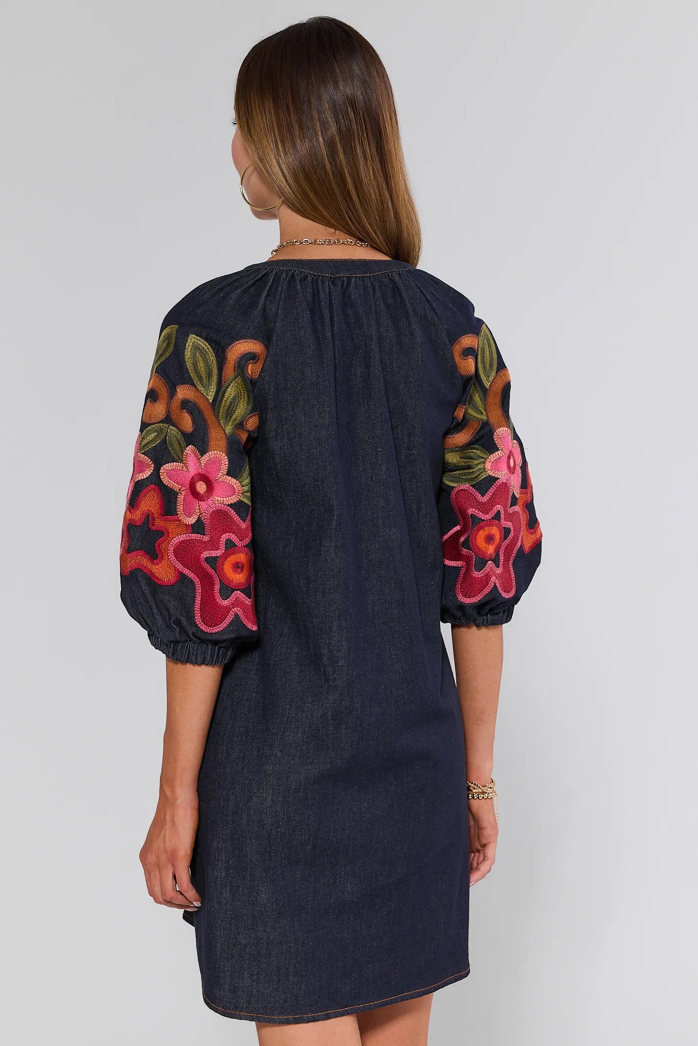 Woman wearing a Winnifred Dress with colorful floral embroidery on sleeves against a white background