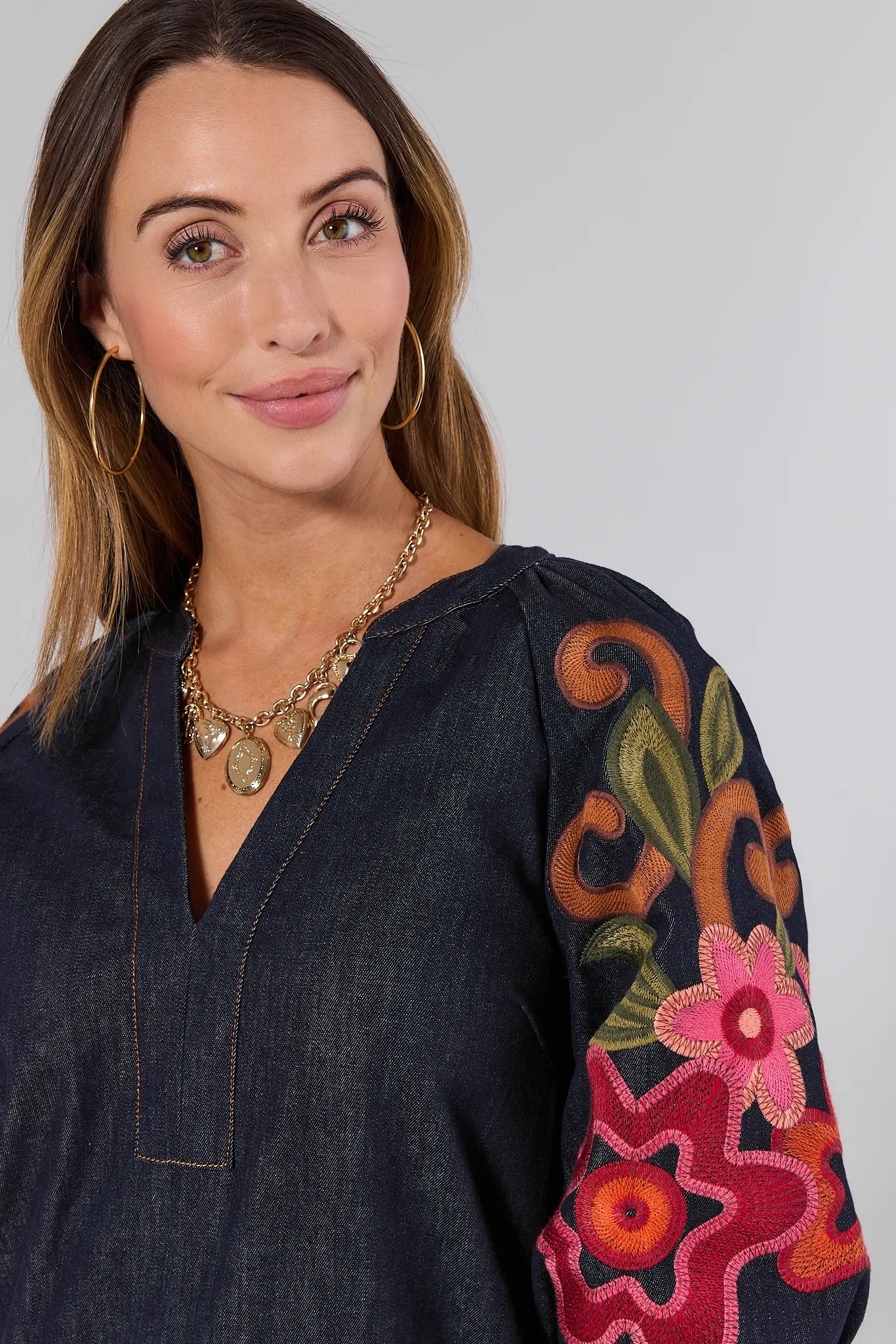 Woman wearing a dark blue Winnifred Dress with colorful floral embroidery on sleeves against a plain background