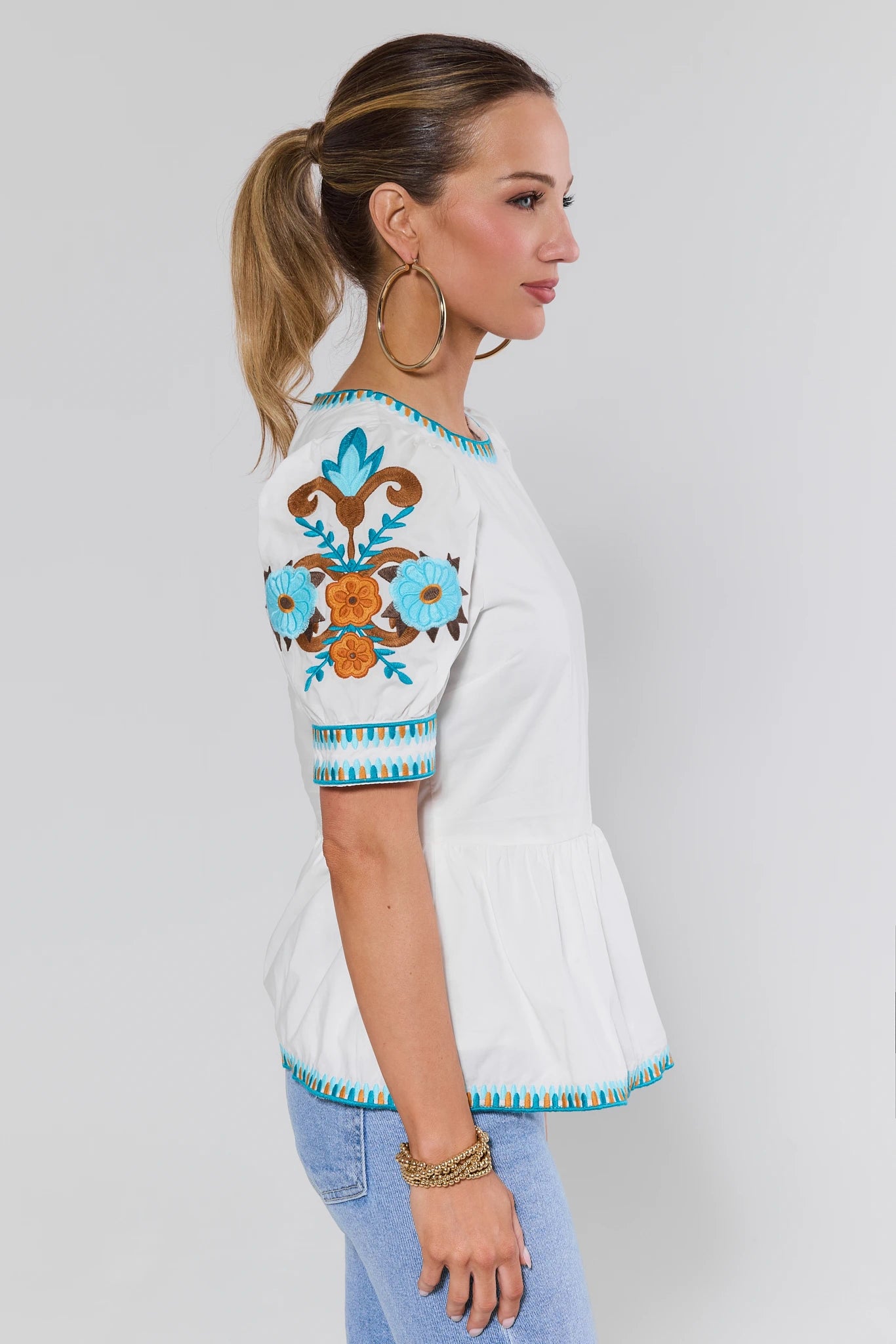 Woman wearing a white top with colorful embroidery on a plain background