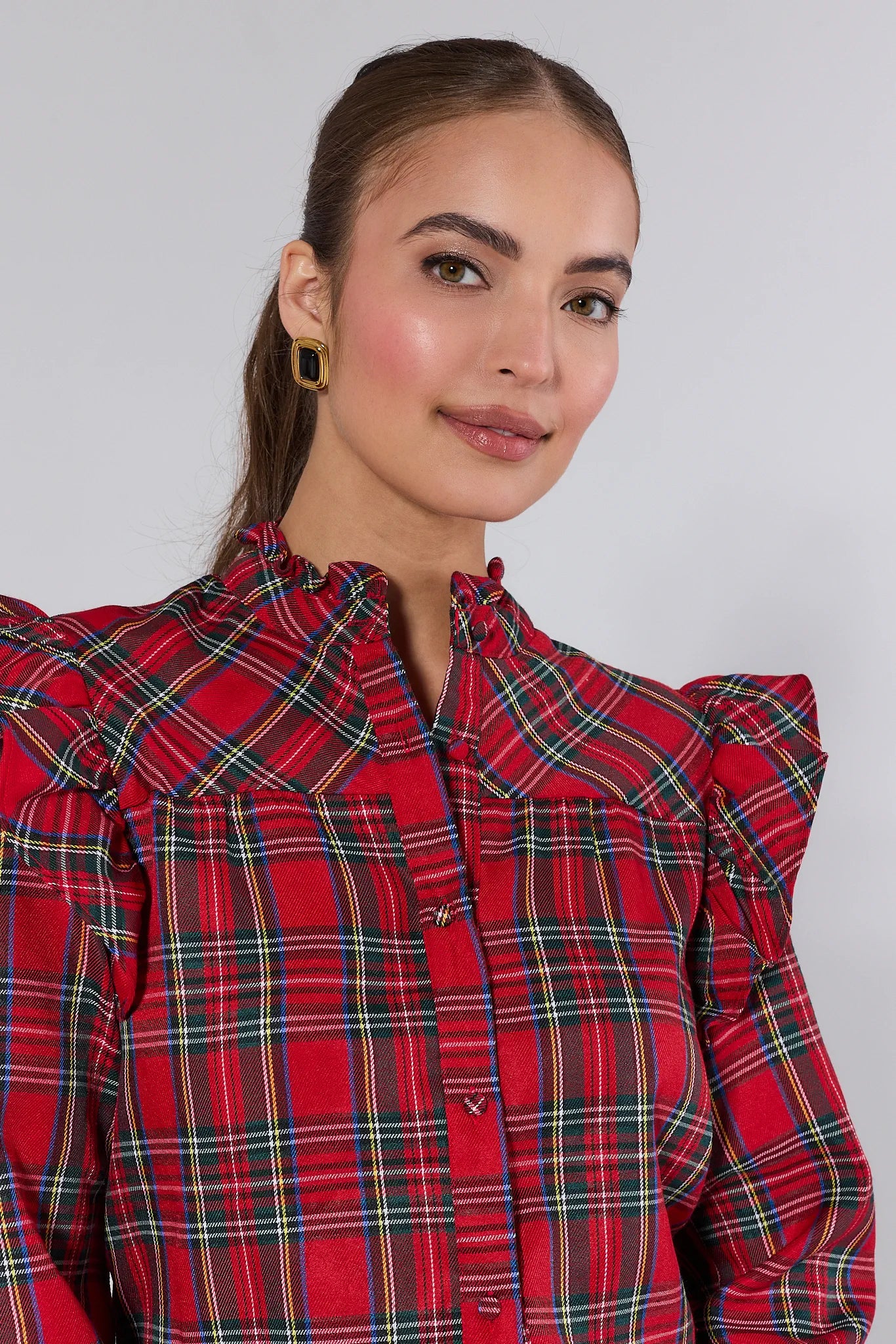 Woman wearing a Holly Plaid Button Up Top with ruffled sleeves and blue jeans, holding a silver clutch.