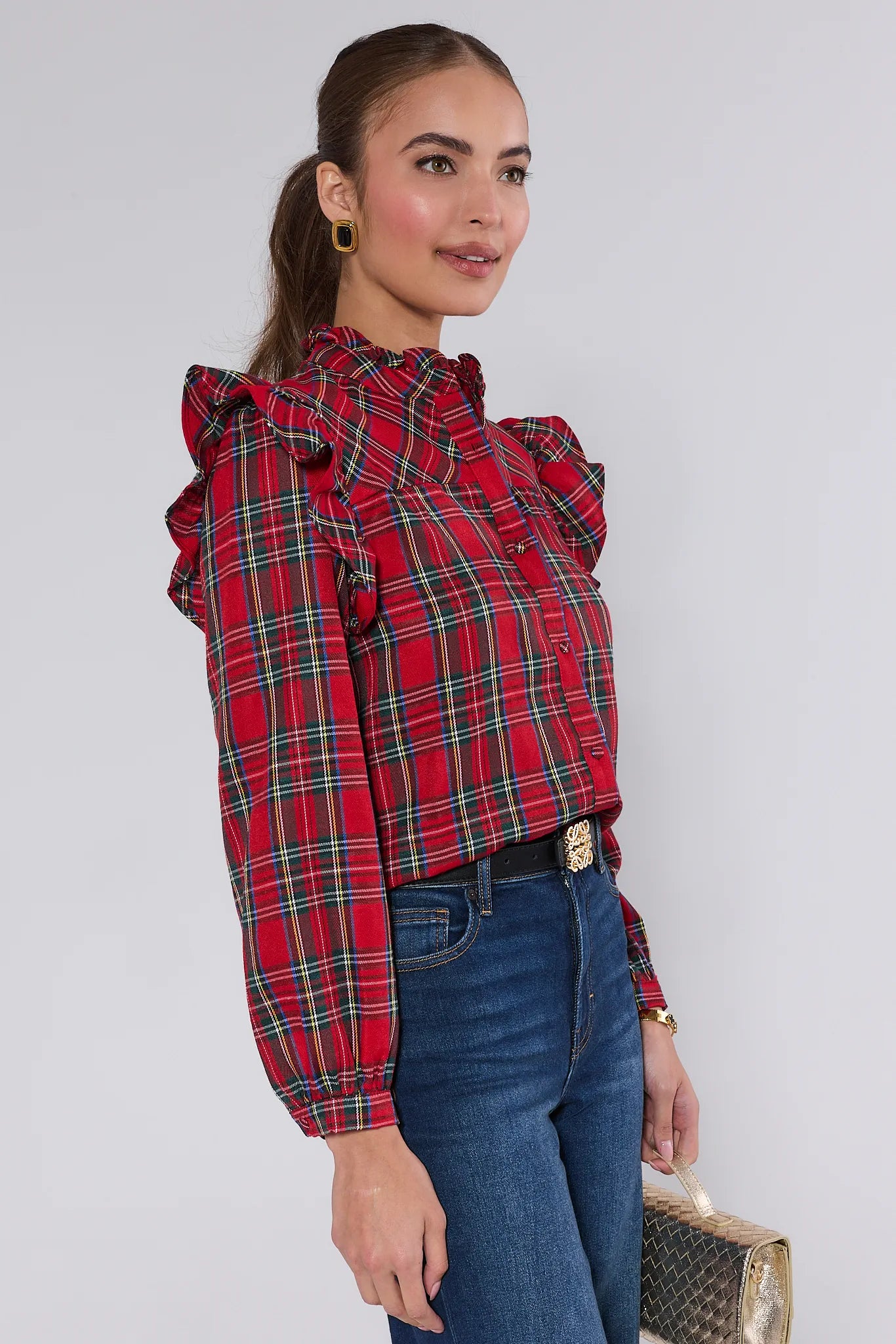 Woman wearing a Holly Plaid Button Up Top with ruffled sleeves and blue jeans, holding a silver clutch.