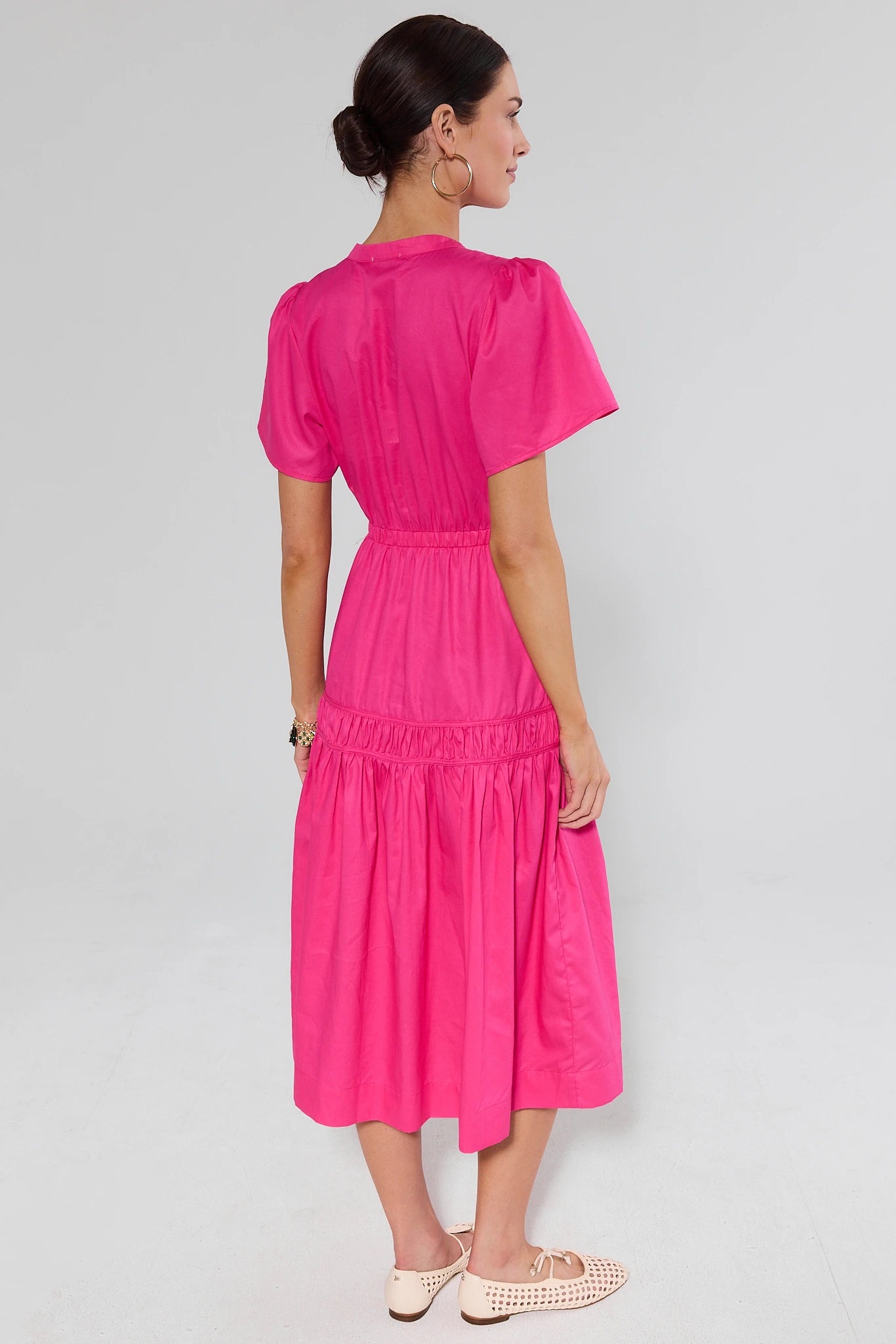 Woman standing wearing a bright pink dress on a light gray background
