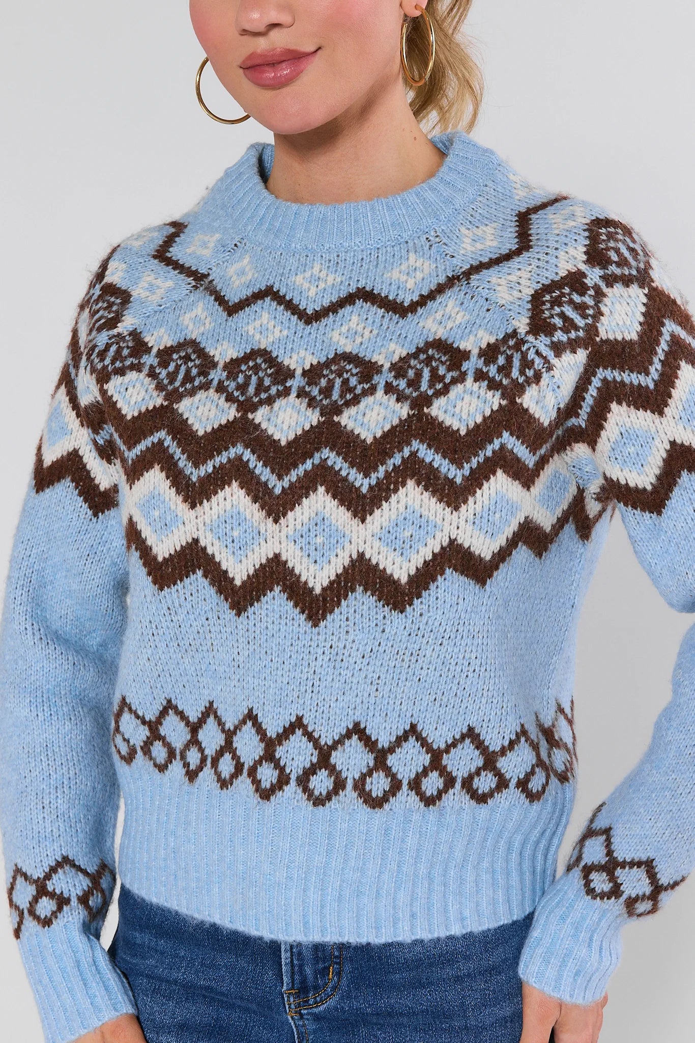 Woman wearing a blue astrid sweater with a pattern, standing against a plain background