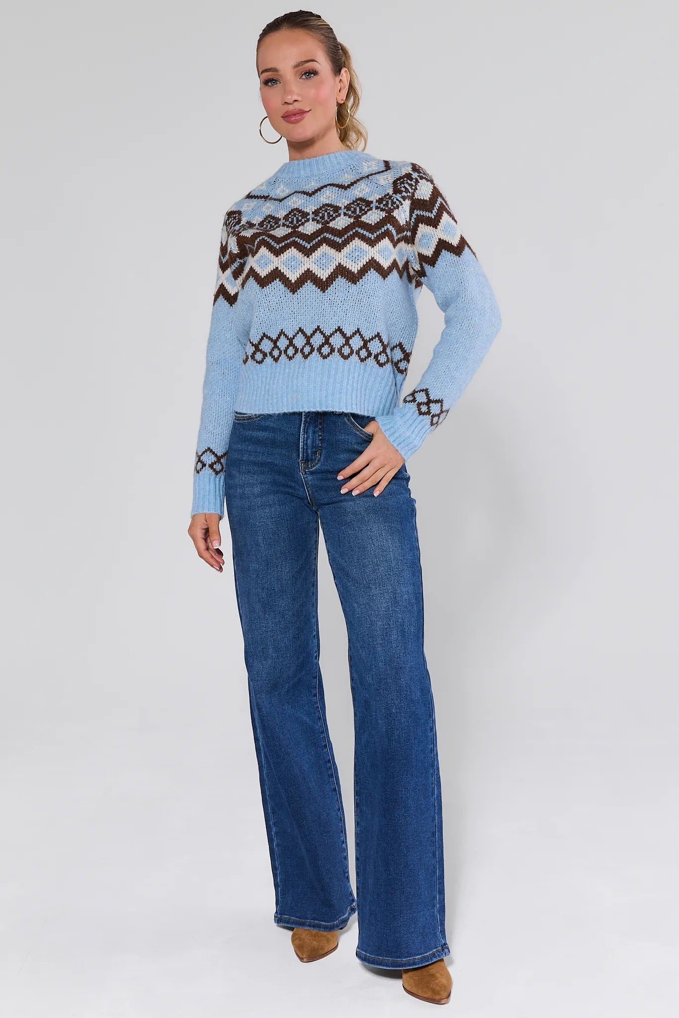 Woman wearing a blue astrid sweater with a pattern, standing against a plain background