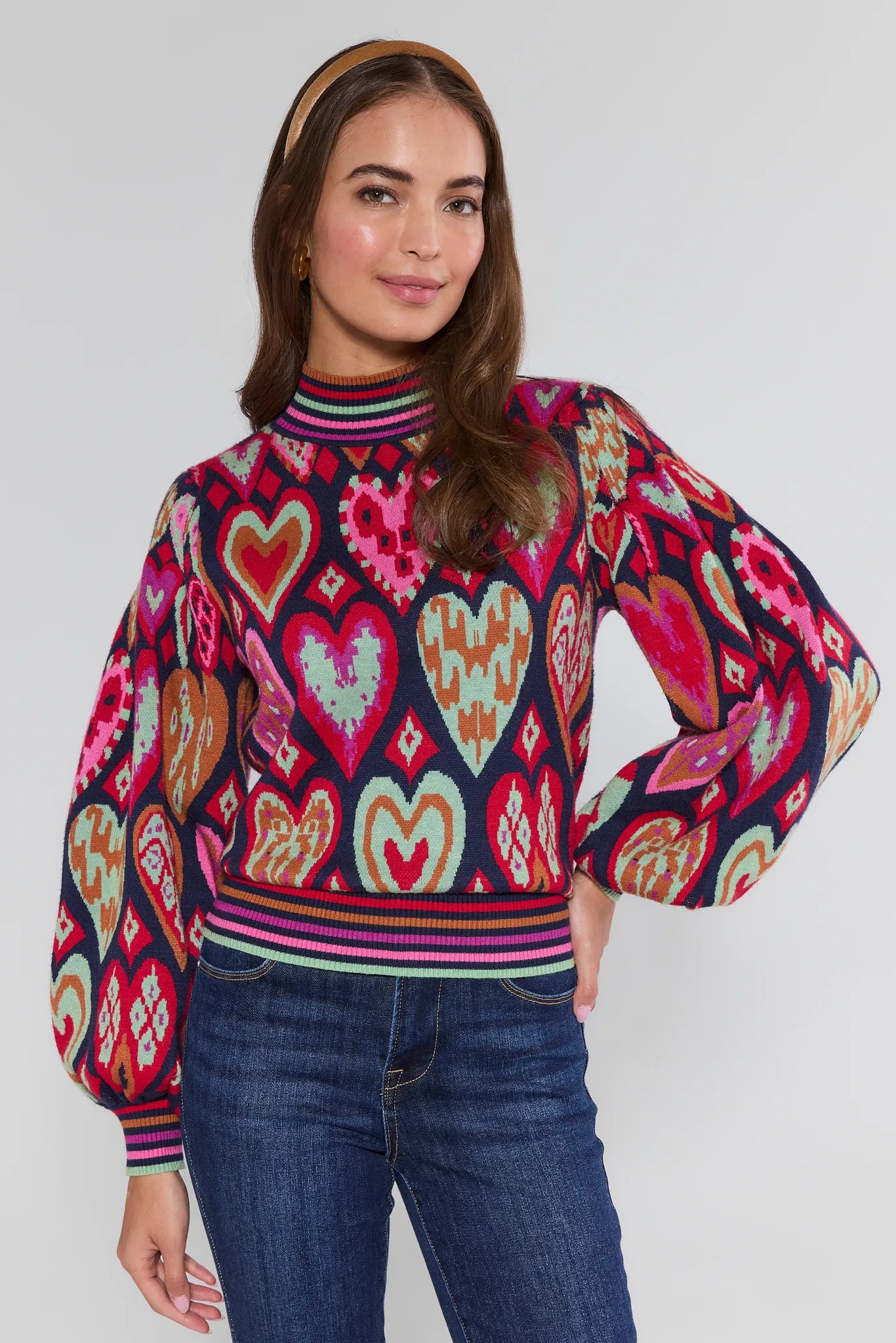 Woman wearing a colorful heart-patterned Maddie sweater against a plain background