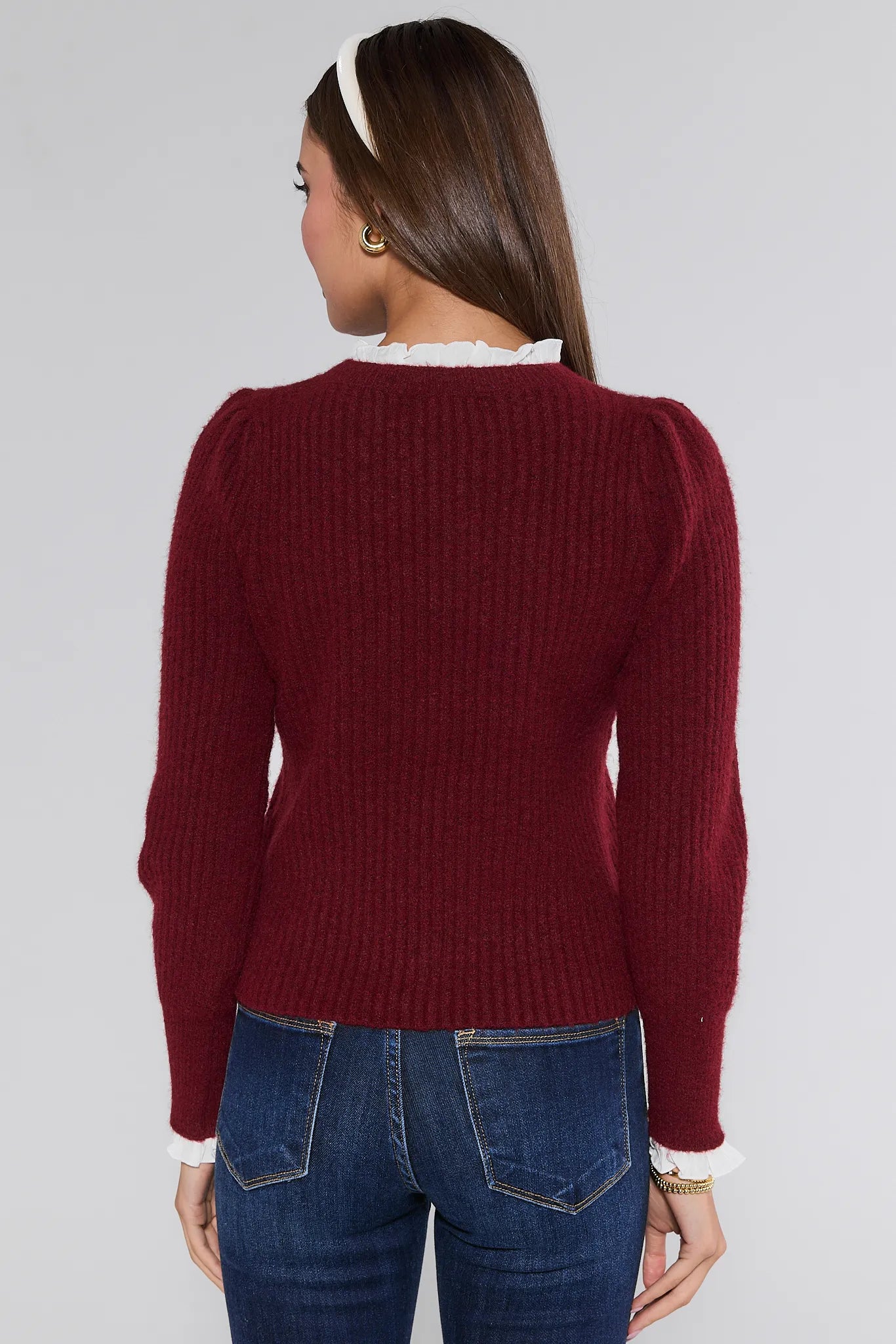 Person wearing a burgundy Annabelle Sweater and blue jeans on a plain background
