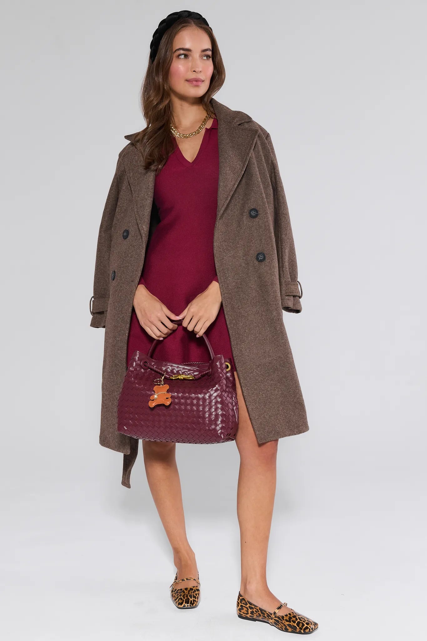 Woman wearing a brown coat over a  Amelia Dress Burgundy with a matching handbag on a white background